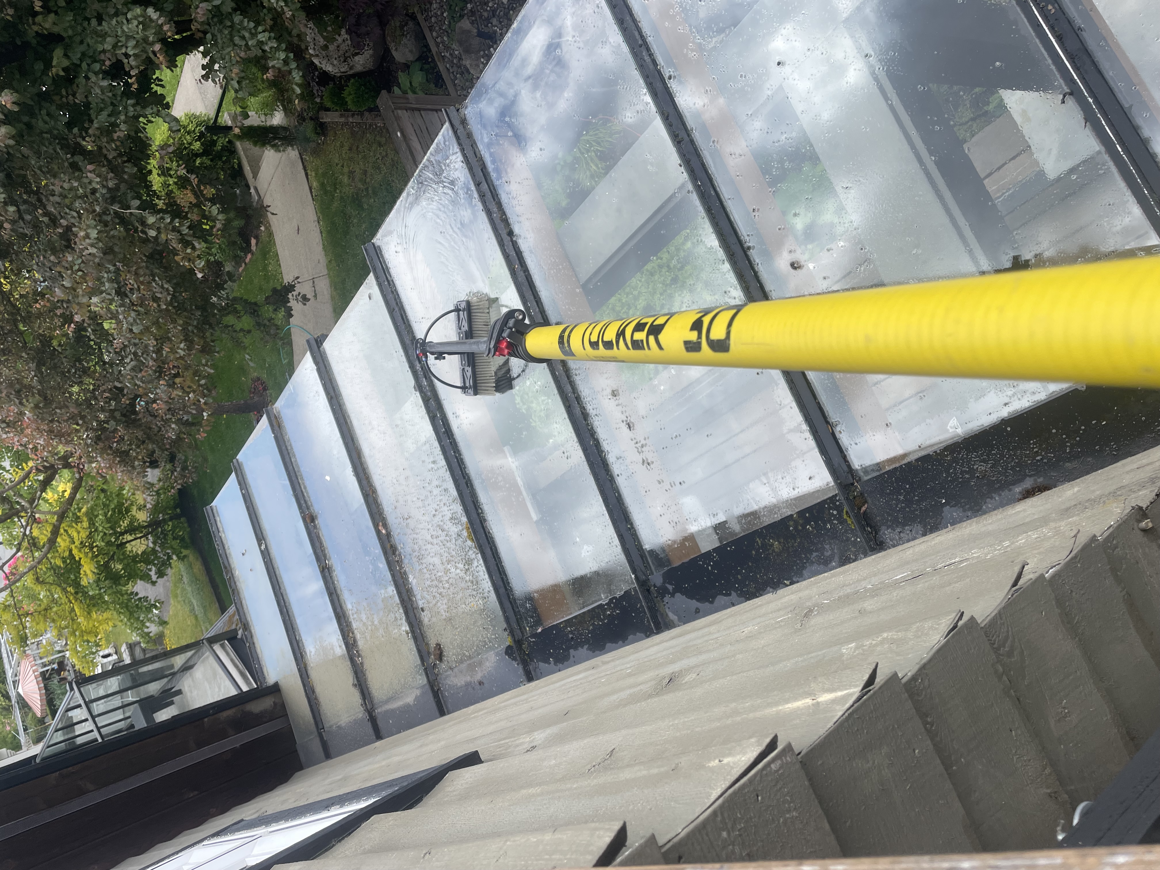 A yellow water-fed pole brush cleaning large glass skylight panels