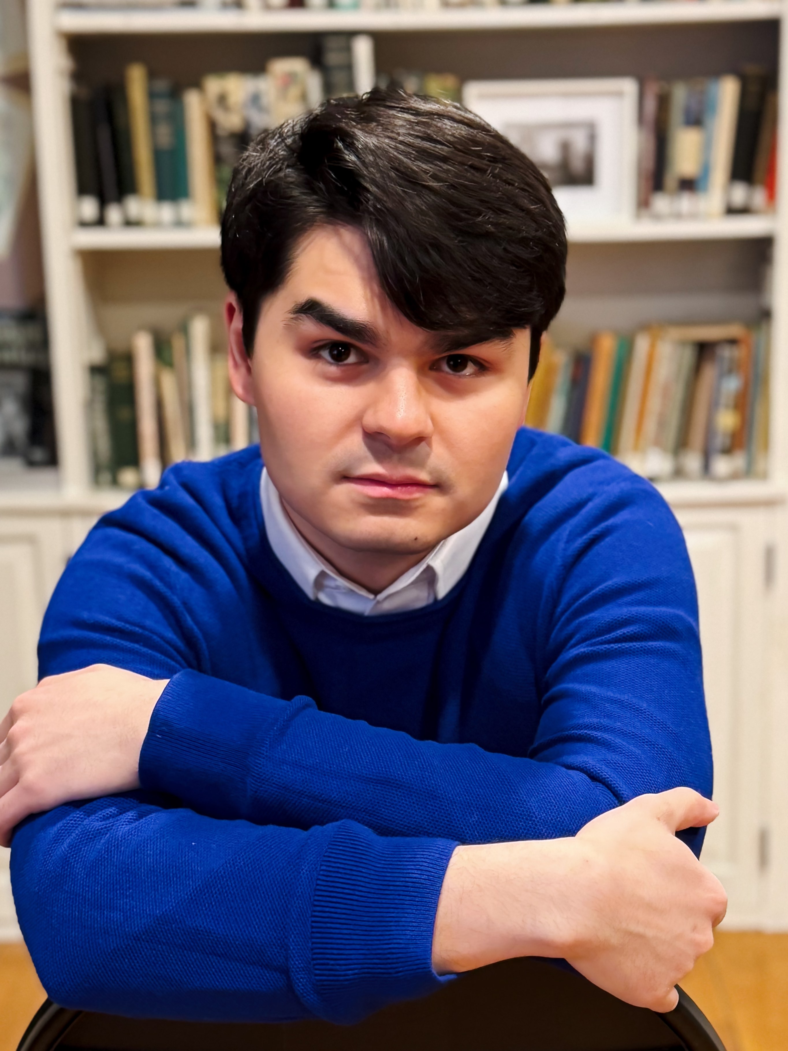 Avery Scott portrait in blue sweater with bookshelf