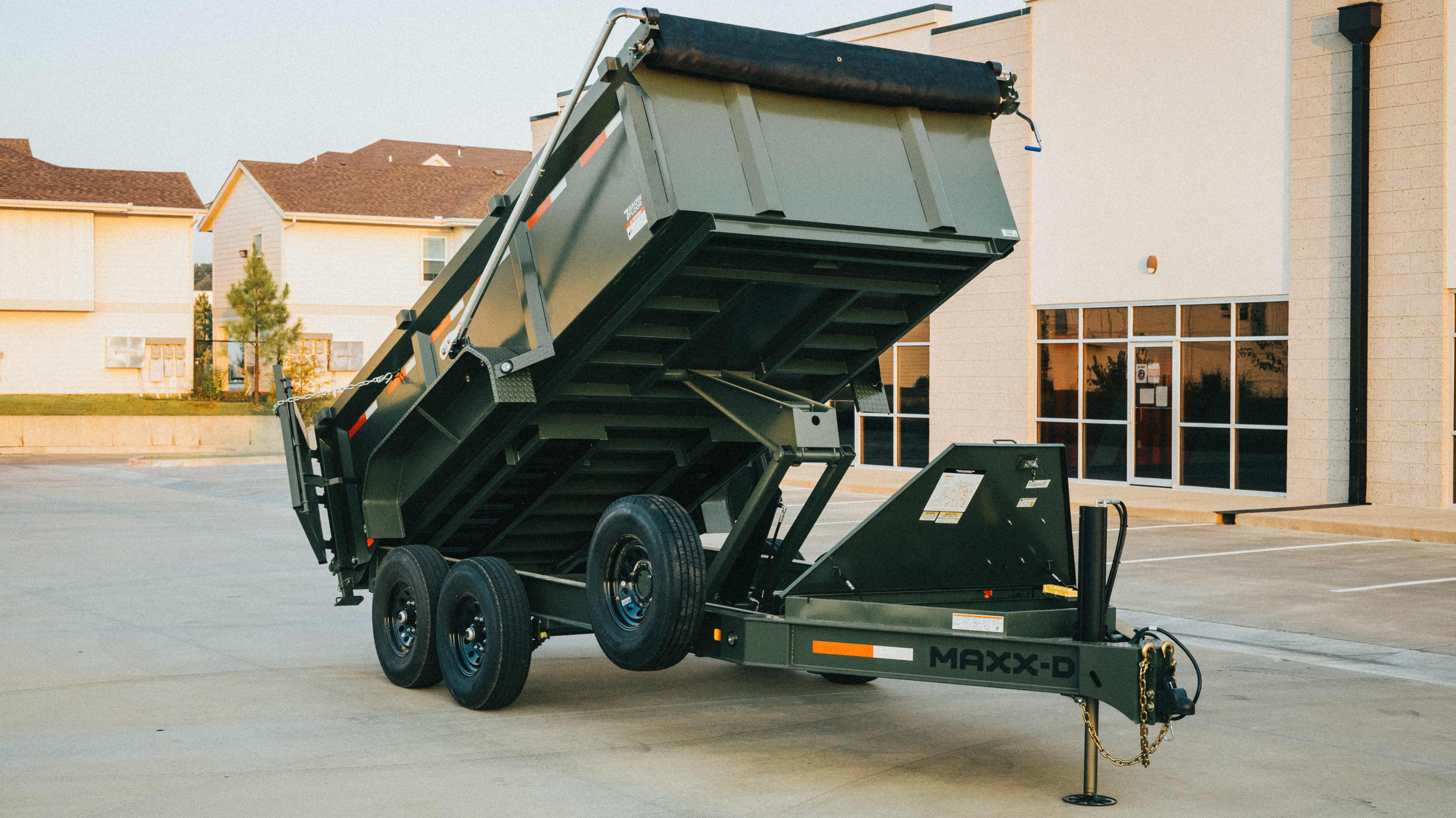 Maxx-D dump trailer with bed raised and tarp rolled back, dumping in a parking lot