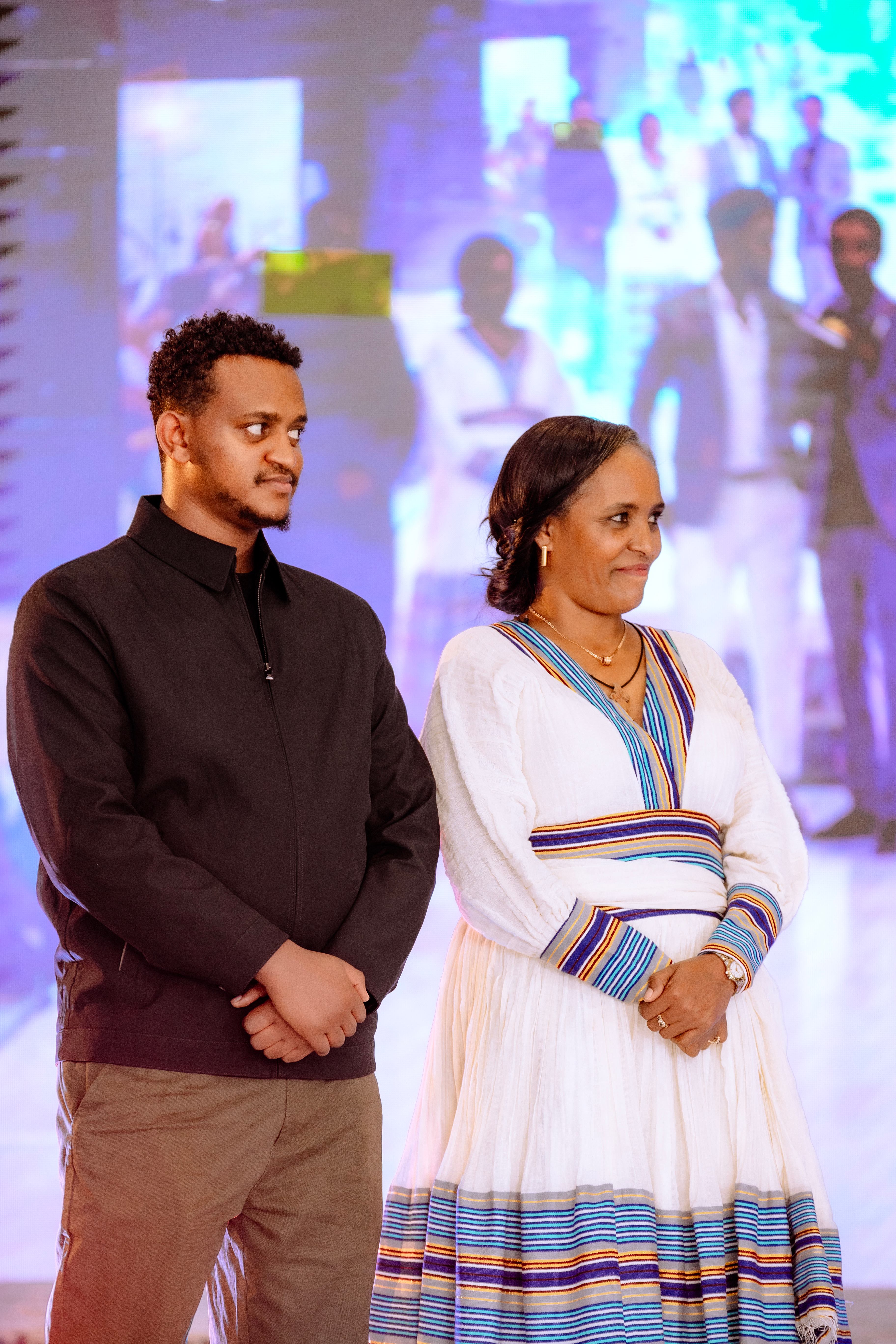 Two presenters on stage in a white and striped look