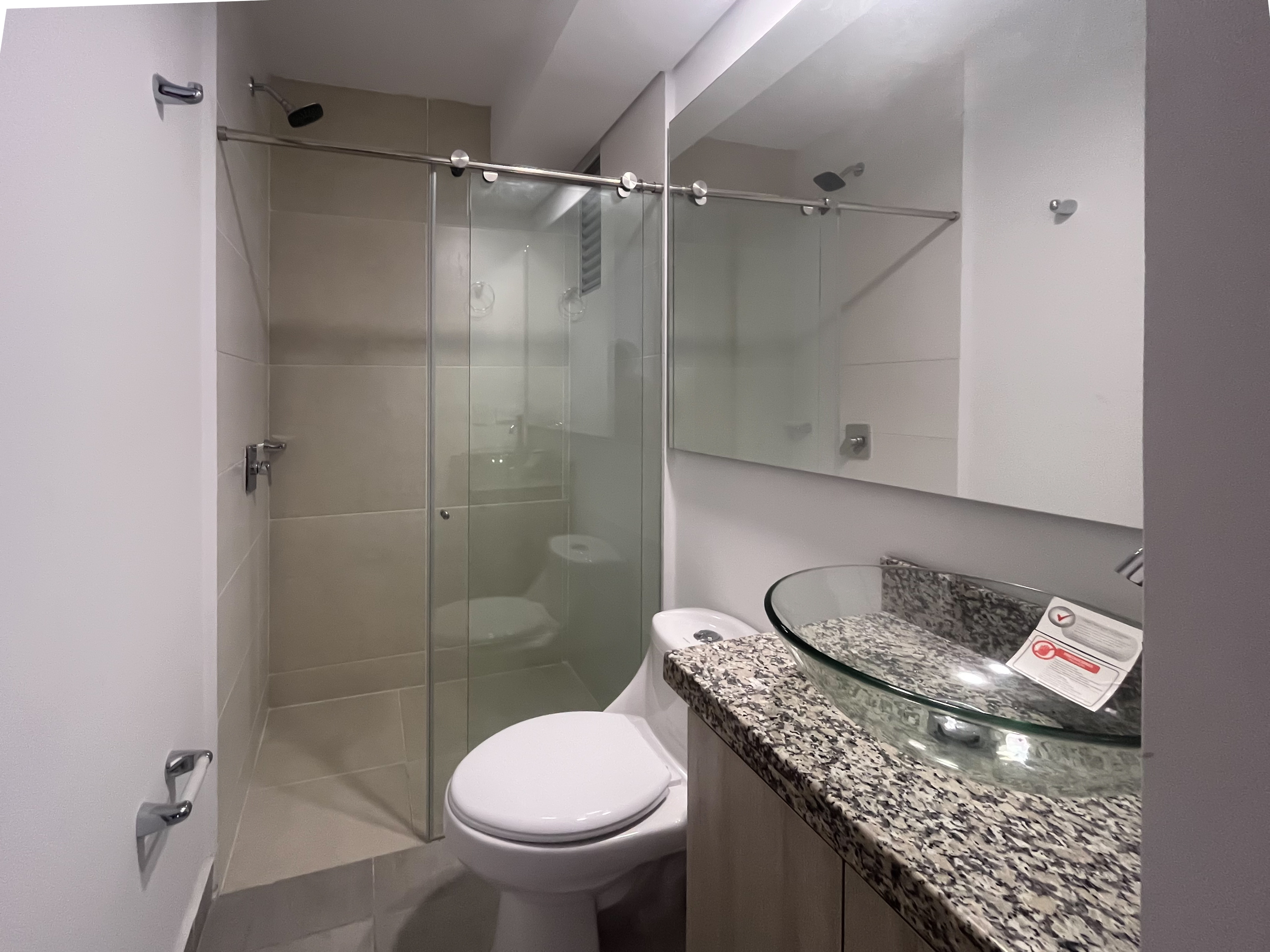 Baño con sanitario elegante y lavamanos de cristal sobre granito