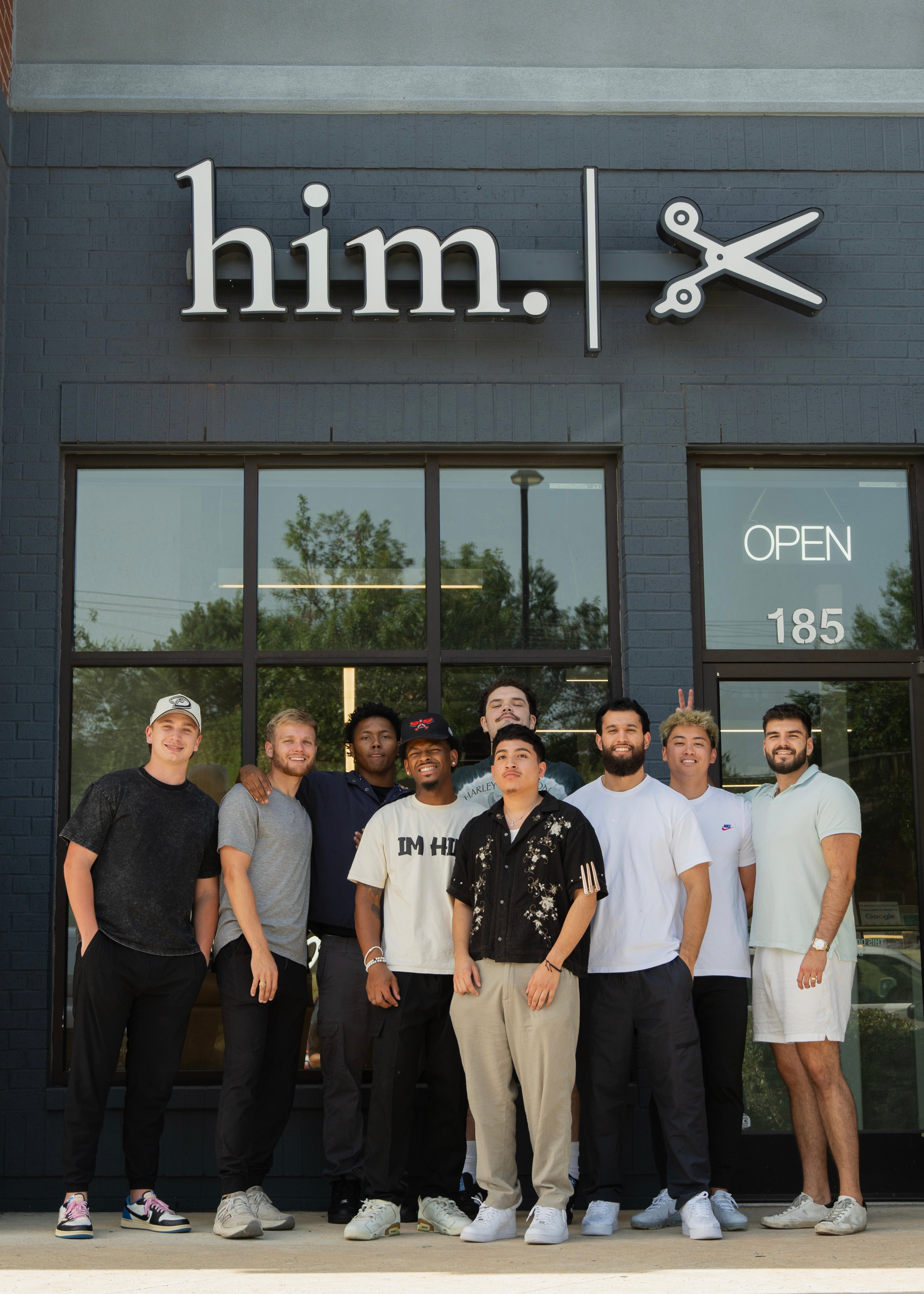 Group of professional barbers standing together in front of a modern barbershop