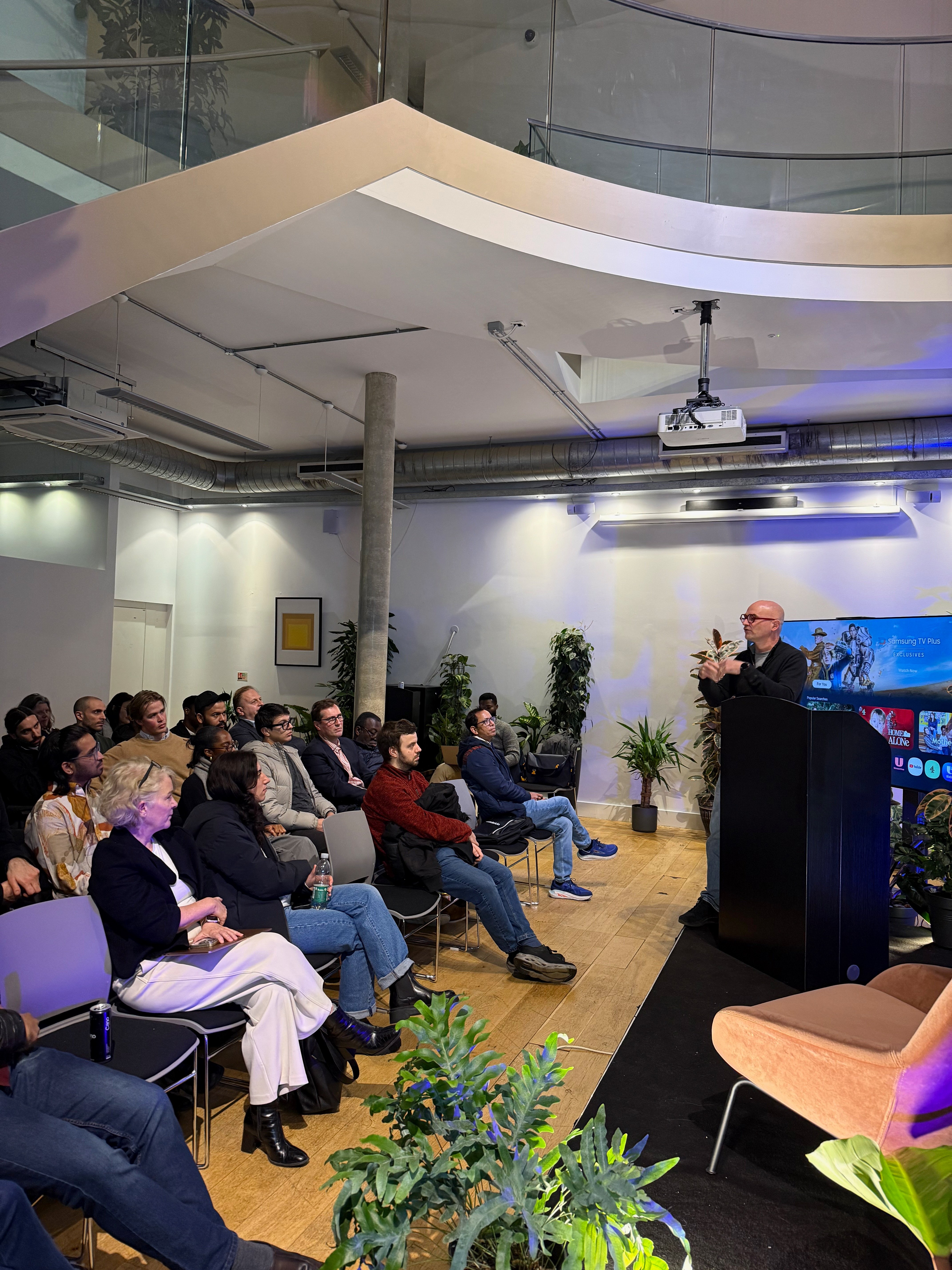 Presenter at podium in a bright atrium venue with mezzanine level
