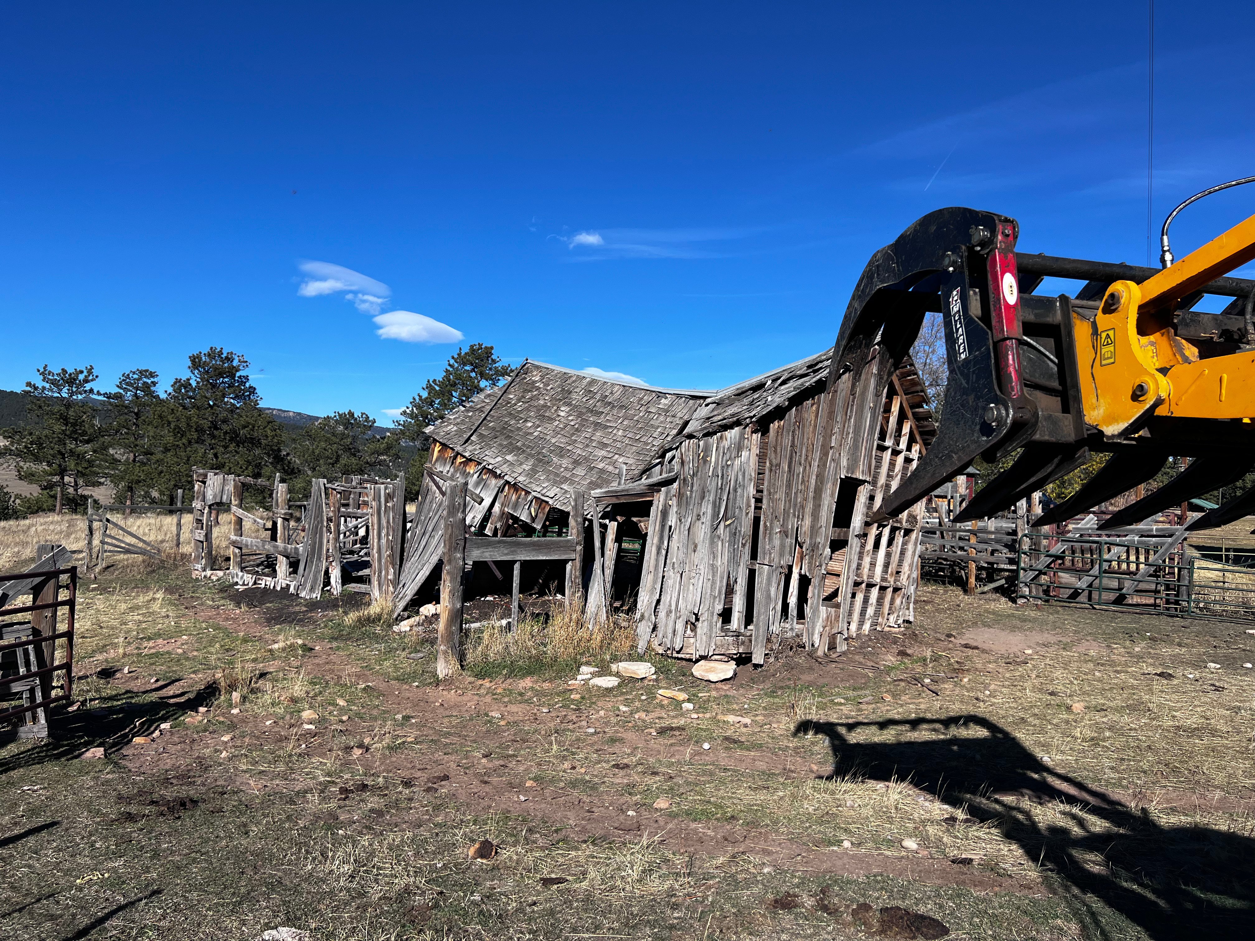 Old barn demolition with excavator bucket in Colorado mountains