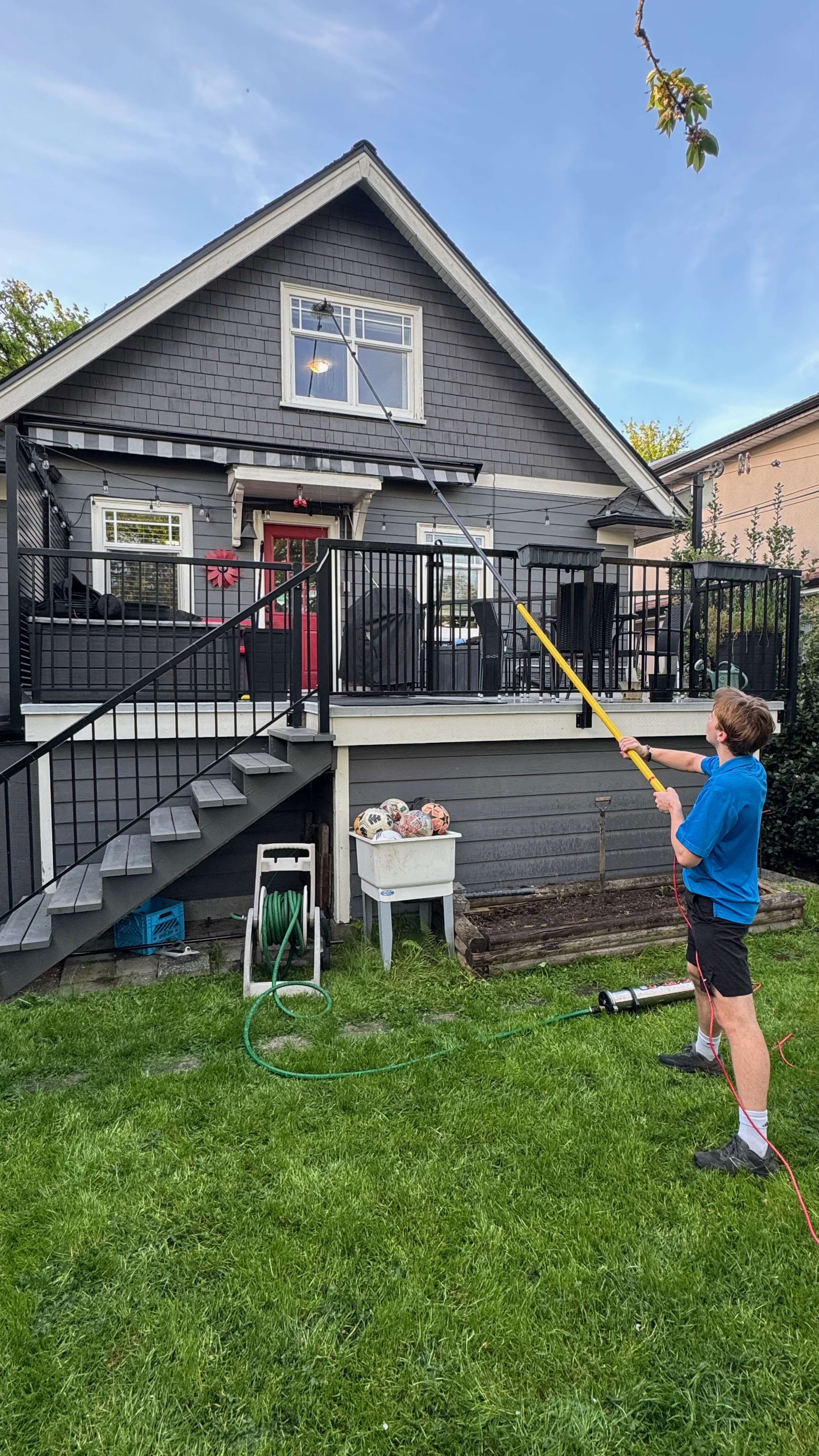 Chris cleaning upper windows from the backyard of a charming grey house with a red door