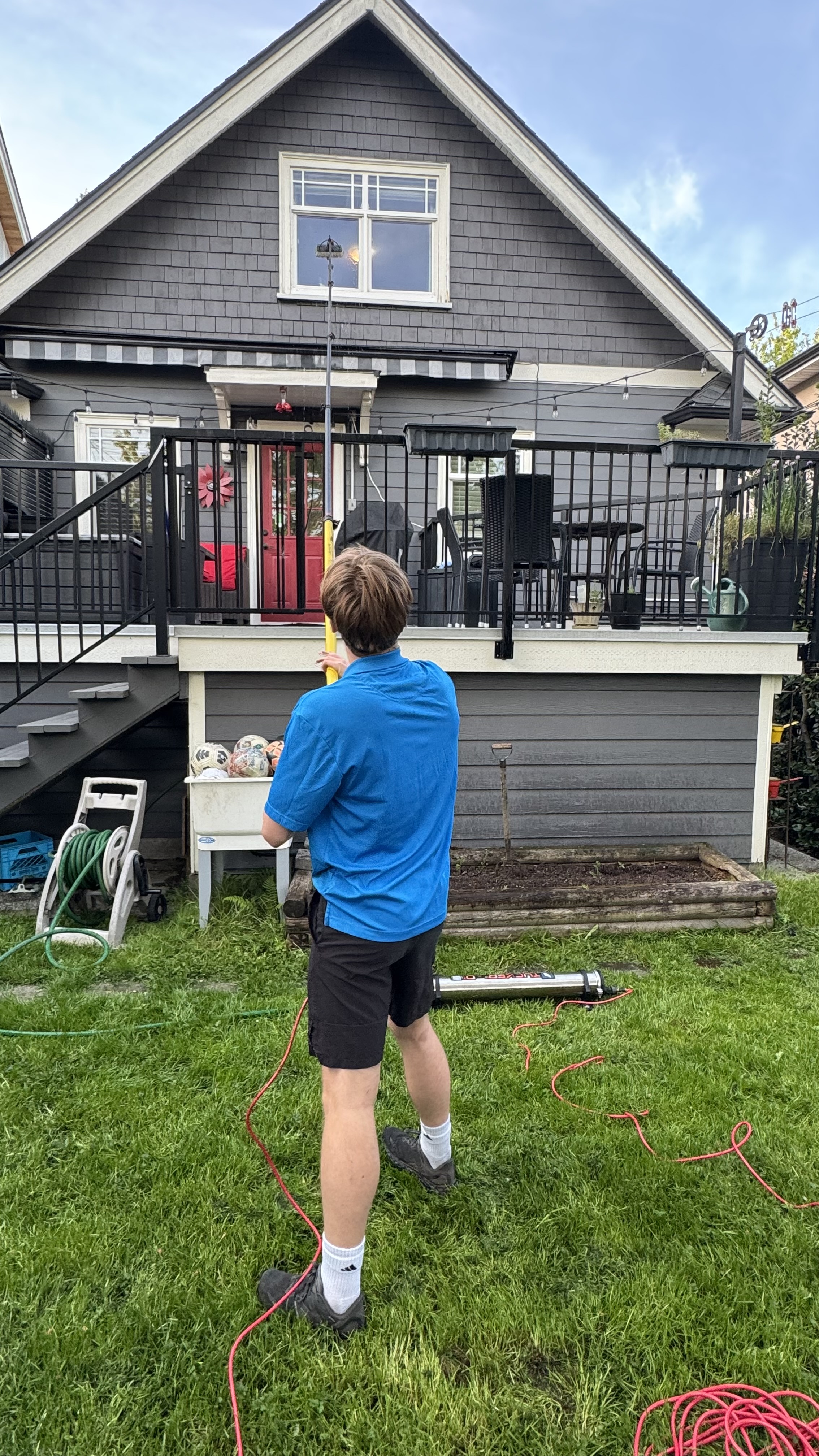 Chris using a tall water-fed pole from the ground to clean a second-storey window