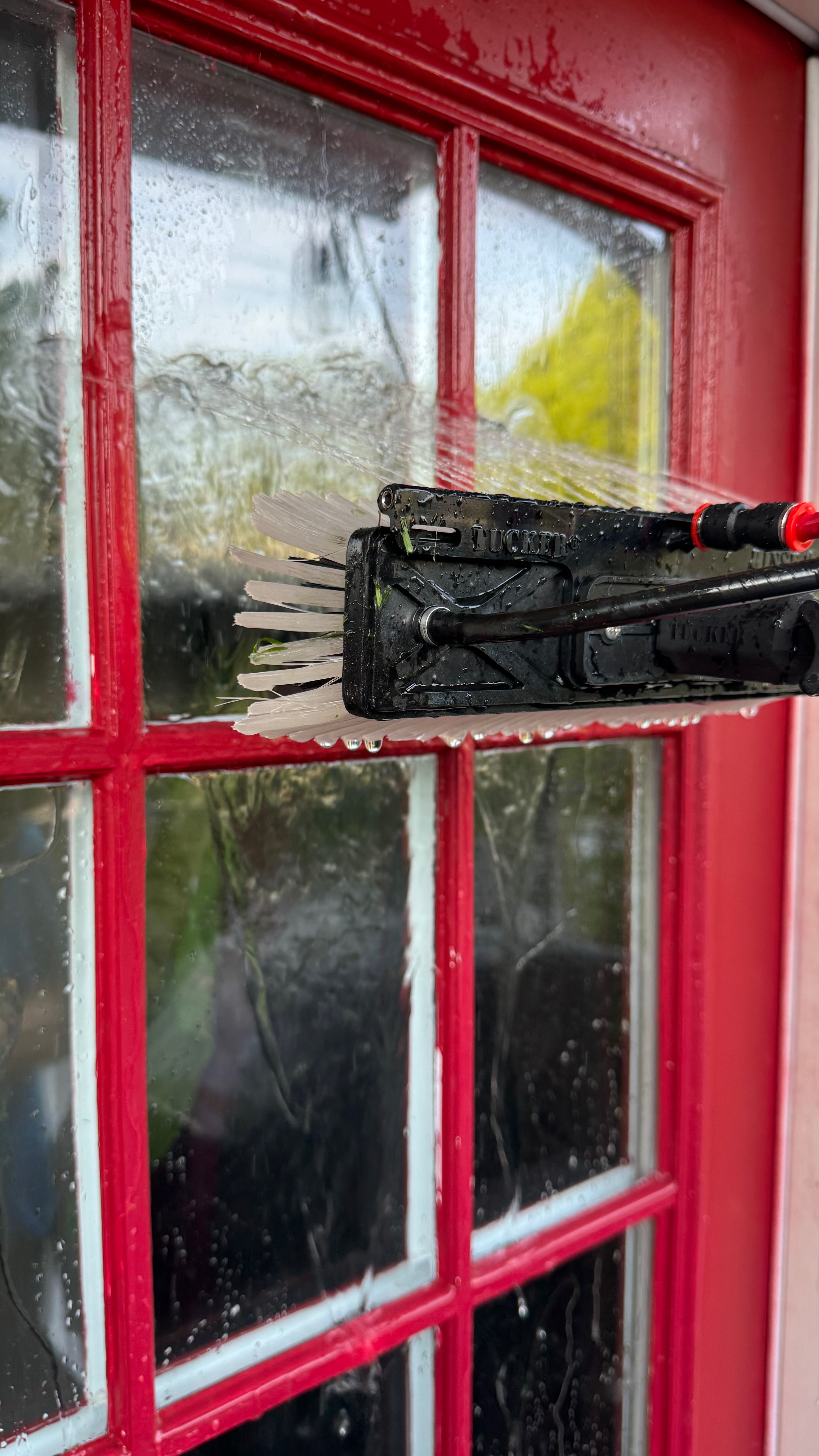 Close-up of the Tucker water-fed brush scrubbing a red-framed window pane