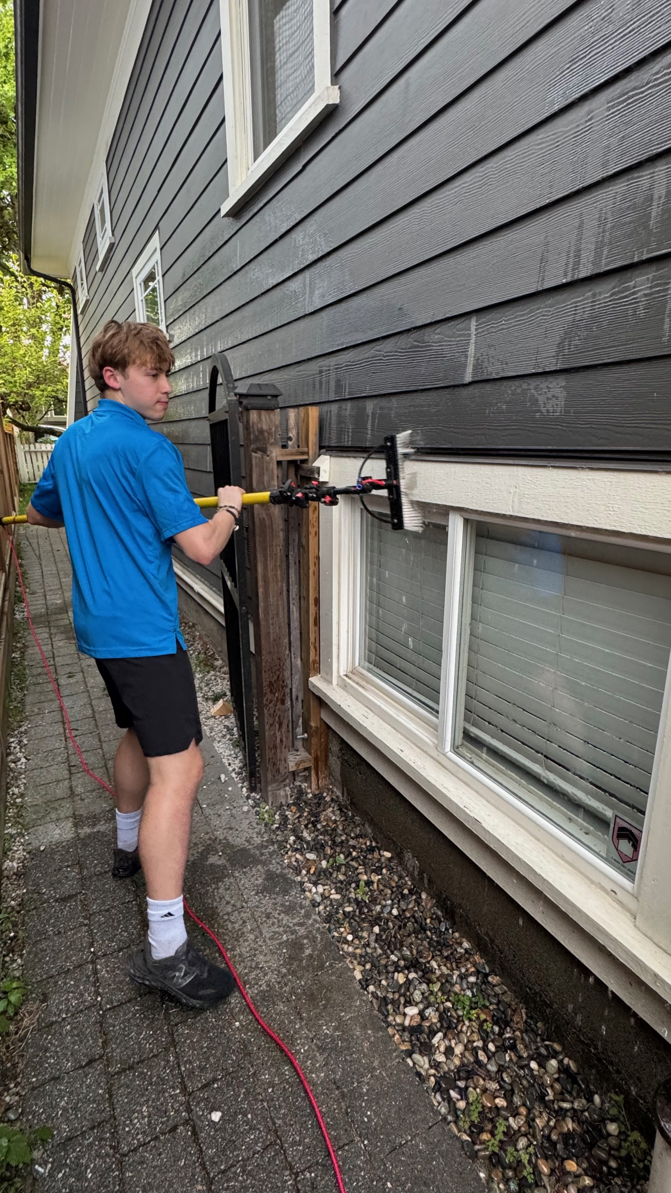 Chris using a water-fed pole to clean ground-level windows on a dark grey house
