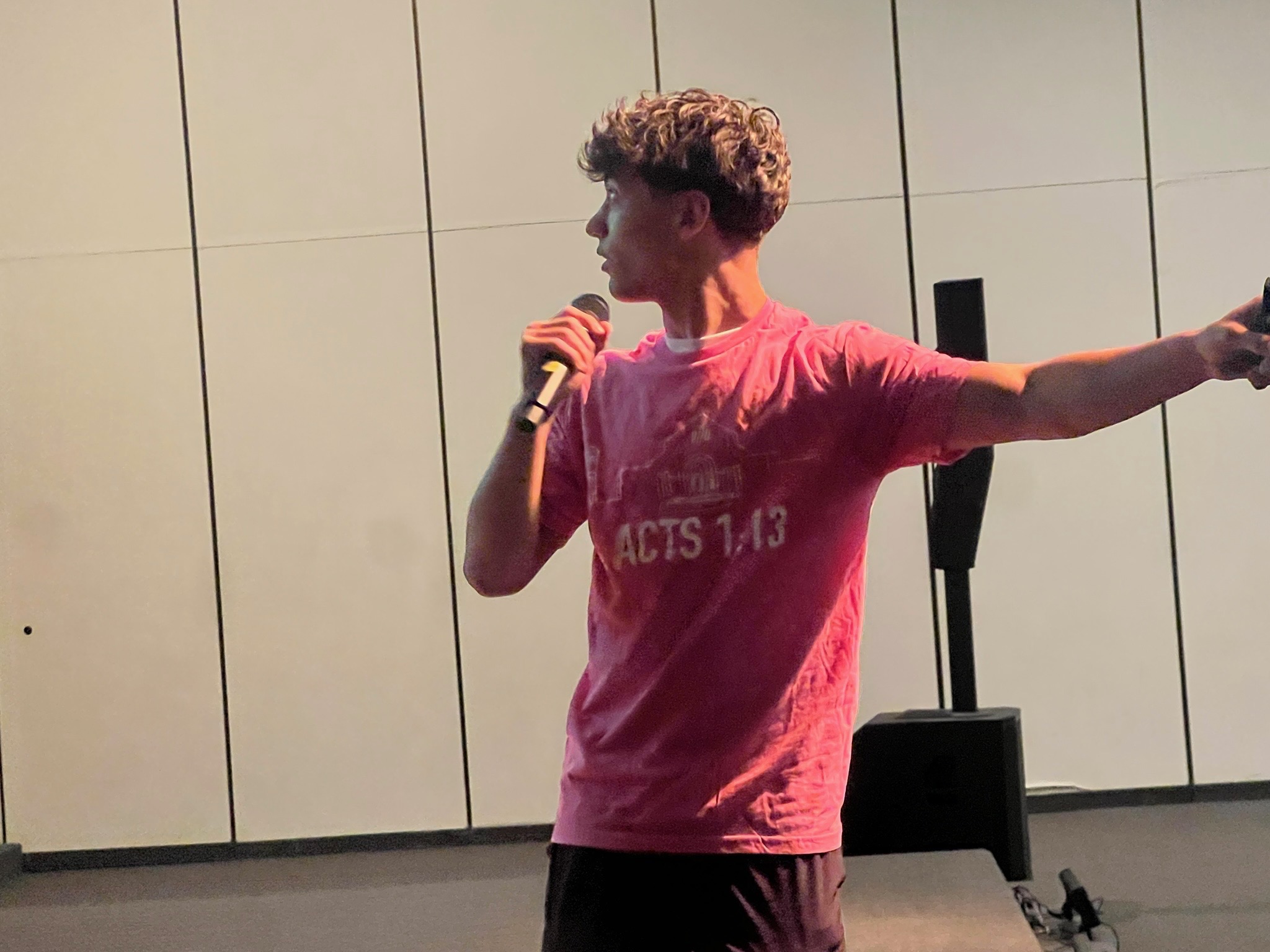 A speaker in an Acts 1:13 shirt addressing a youth group with a microphone