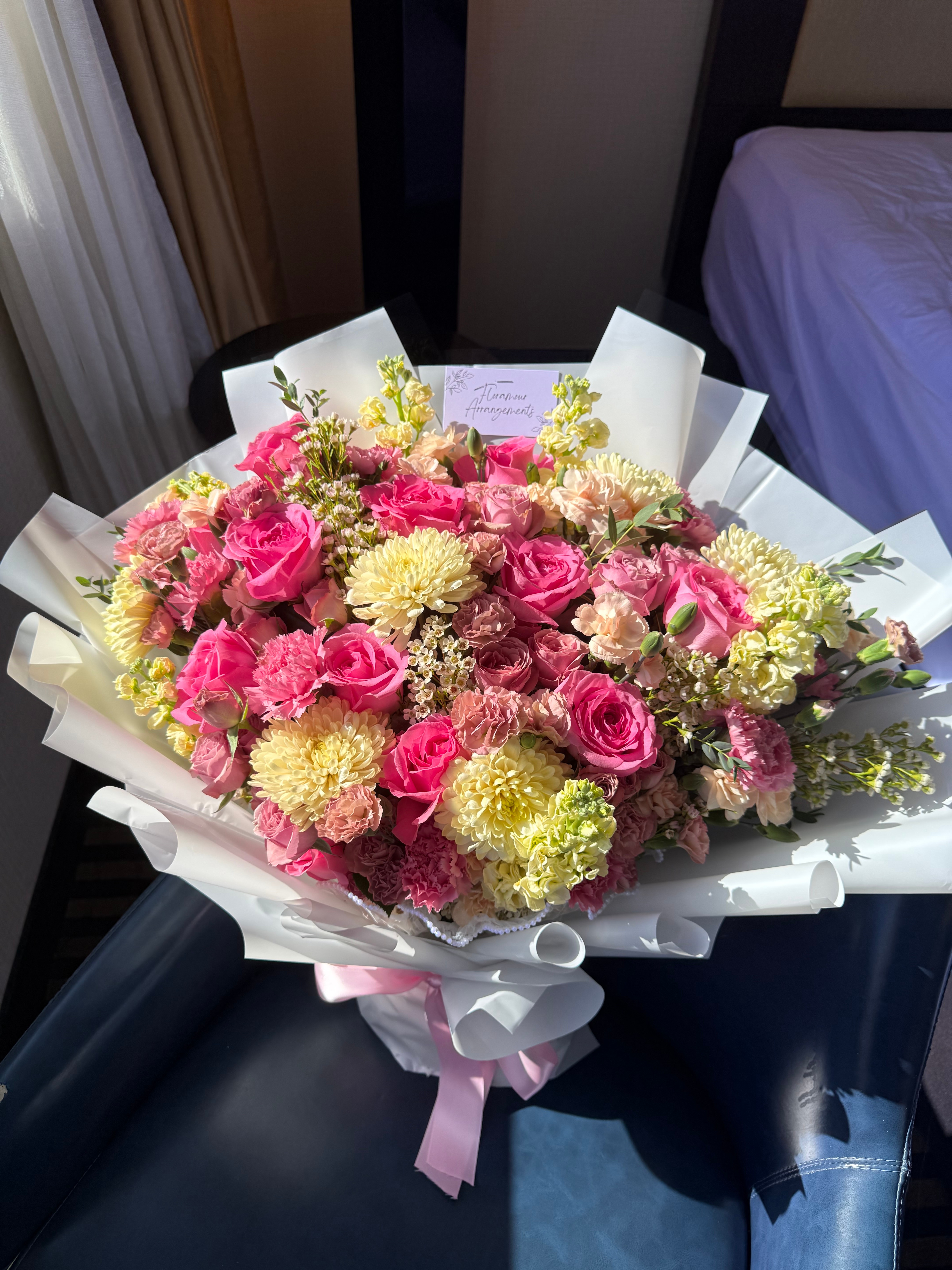 Lush pink roses and cream chrysanthemum bouquet wrapped in white paper with pink ribbon