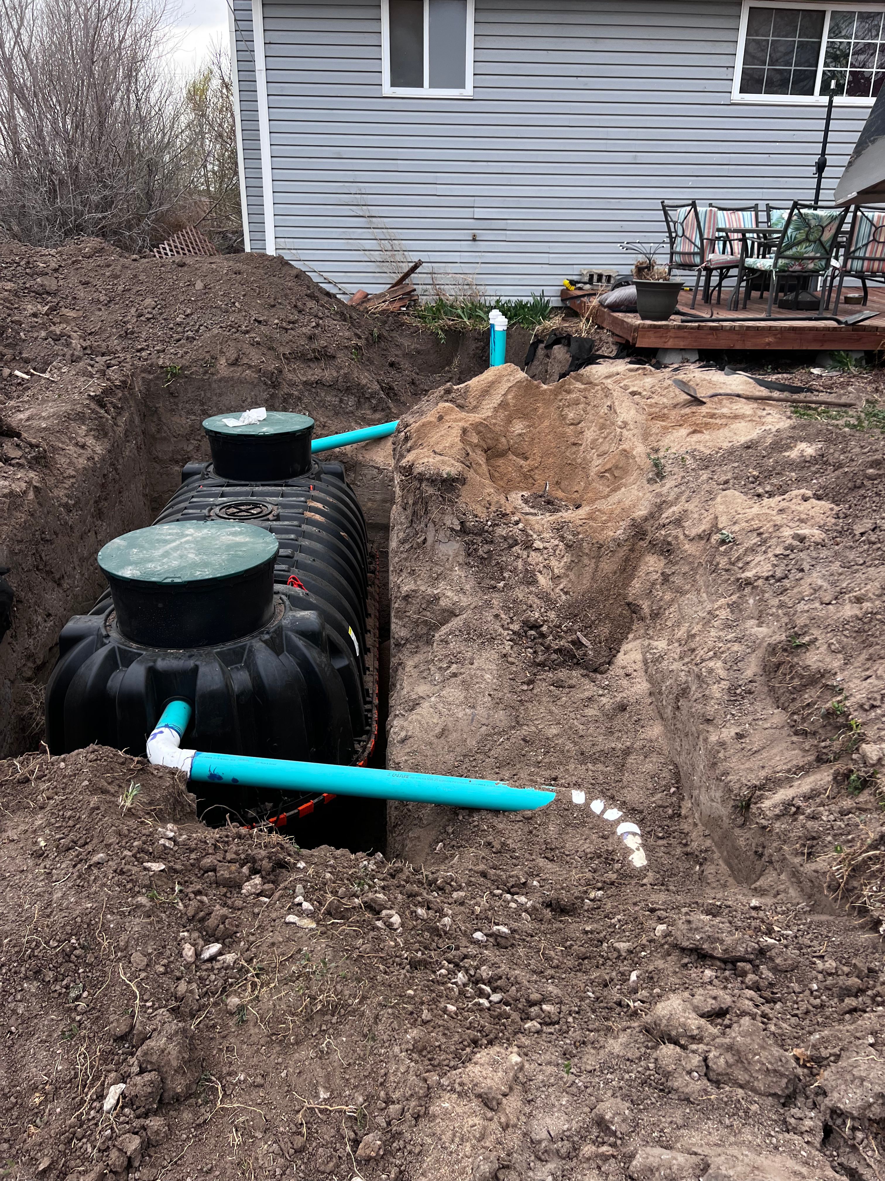 Black septic tank set in excavated pit with PVC piping