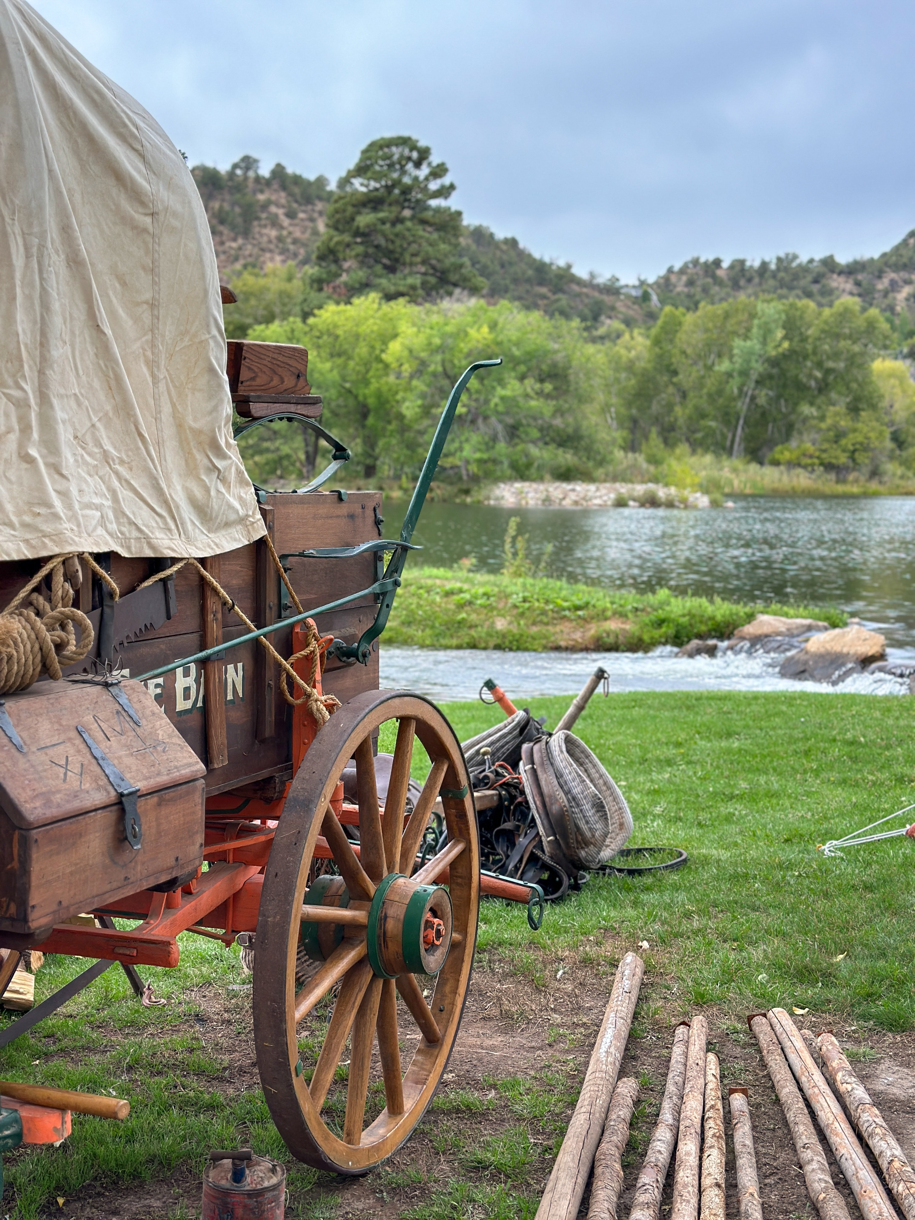Rustic chuckwagon with canvas cover and wooden wheels beside LePlatt's Pond with mountain backdrop