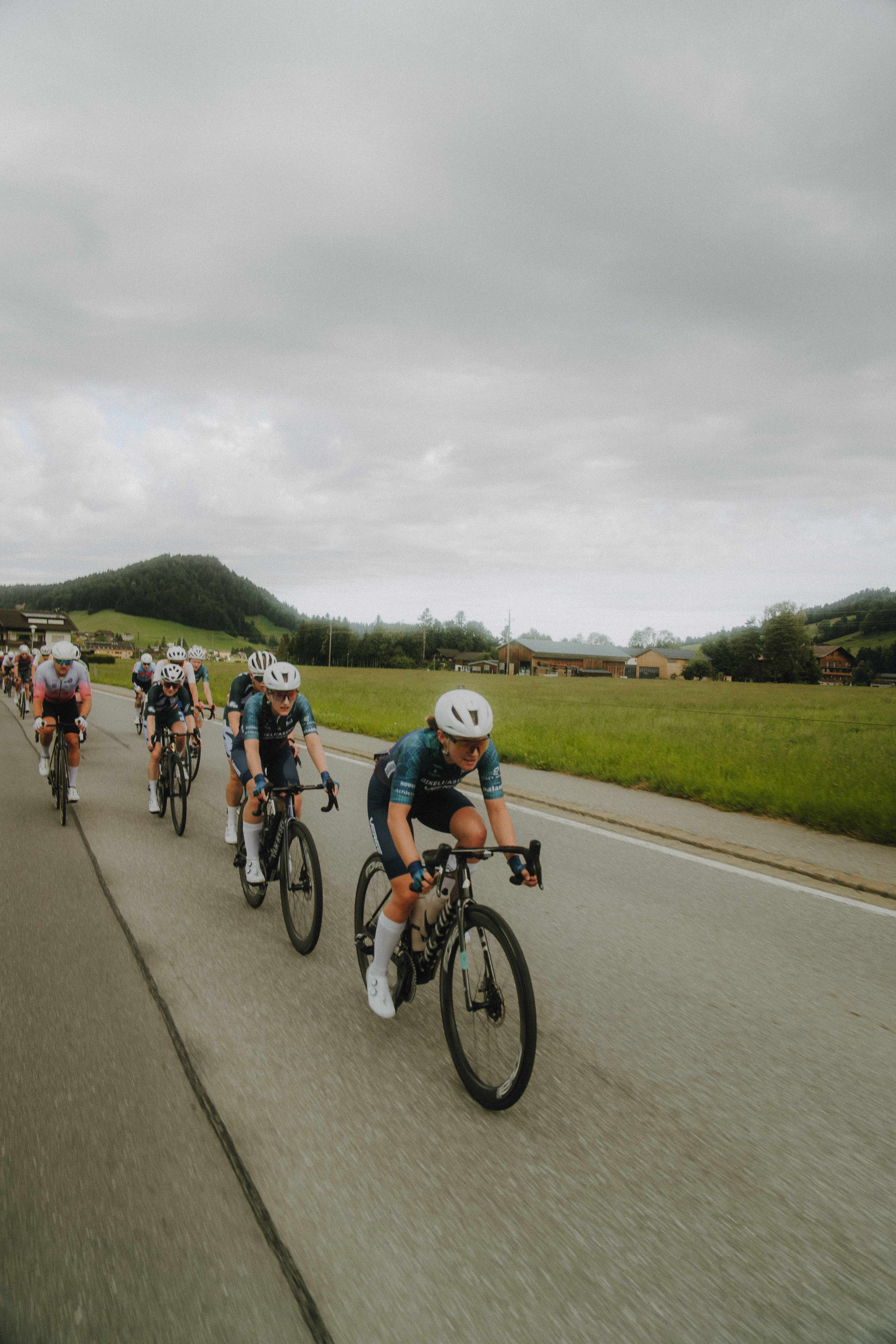 Peloton auf einer Landstraße durch grüne Hügellandschaft