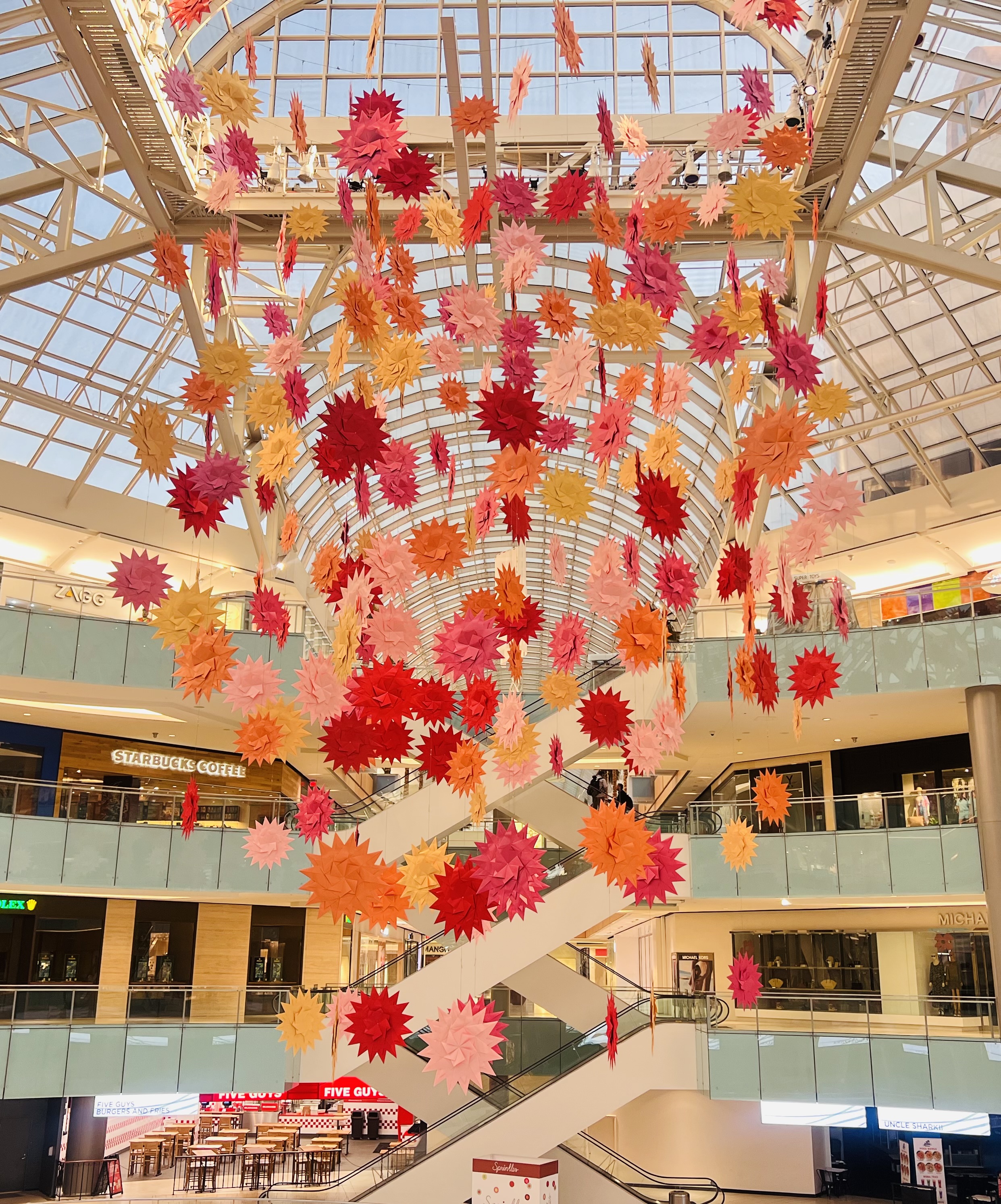 Paper for Water's Folding the Future installation — colorful origami flowers suspended above the Galleria Dallas Ice Rink