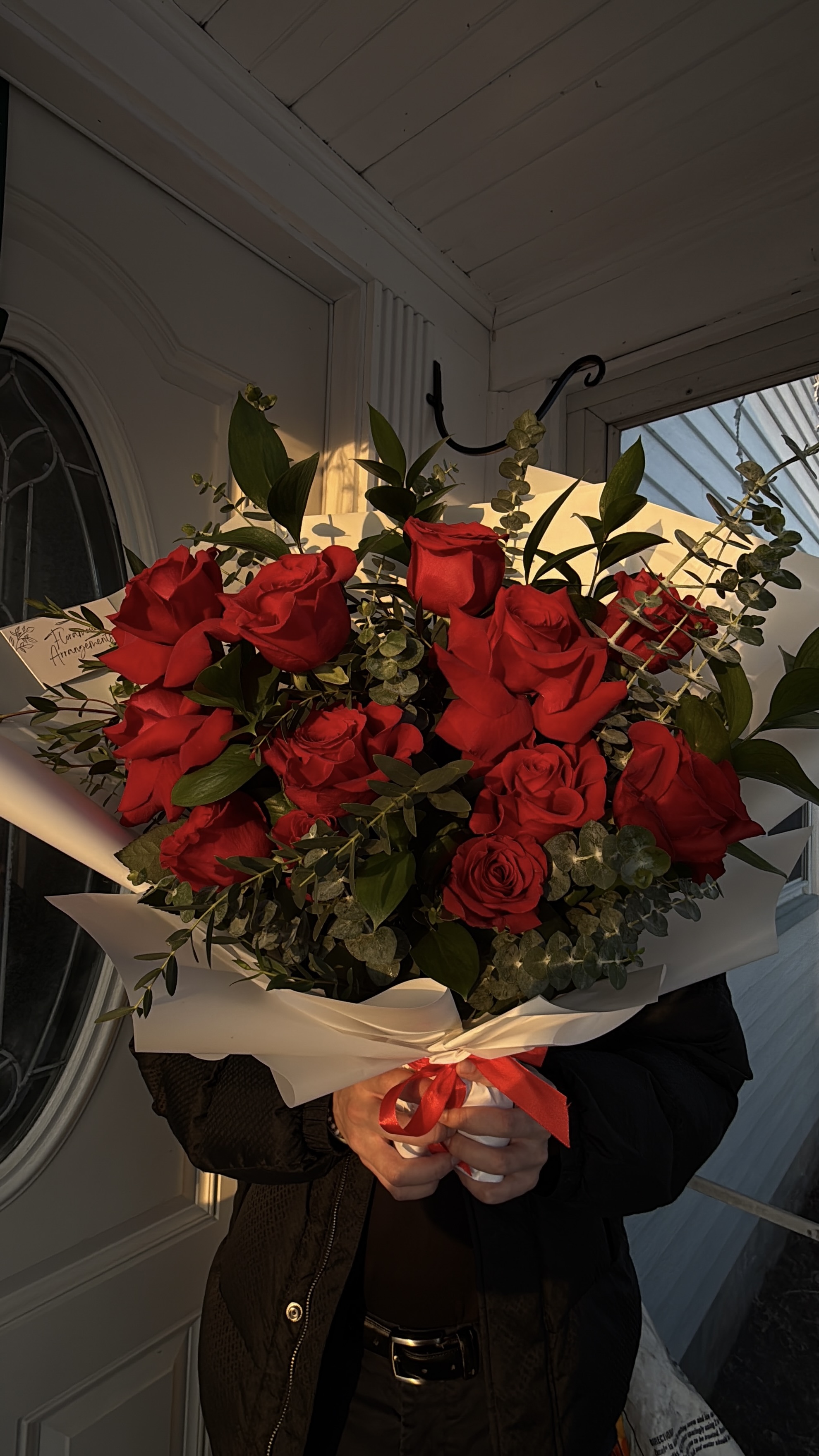 Person holding large red rose bouquet wrapped in white paper with red ribbon