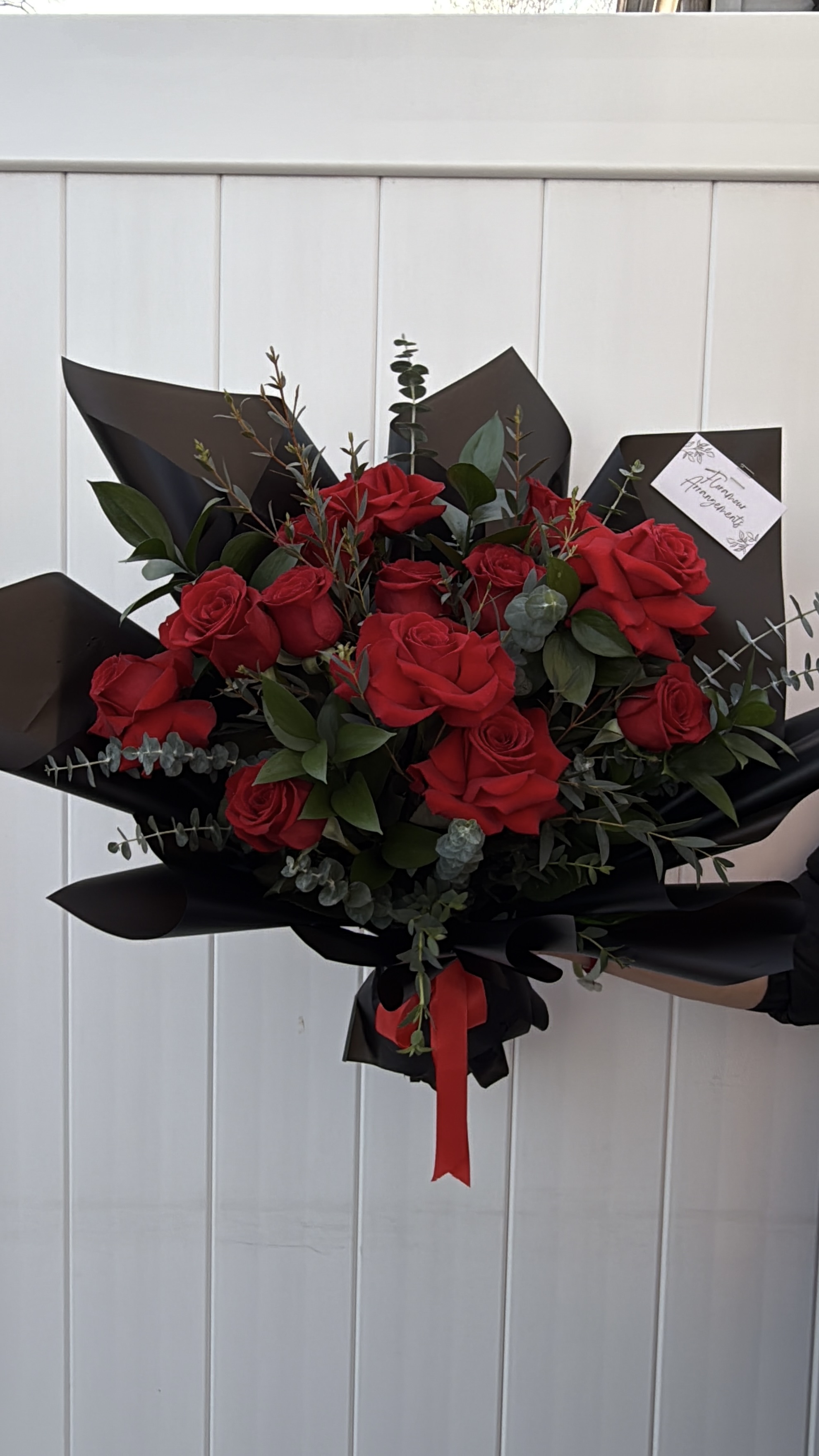 Red roses wrapped in black paper with eucalyptus and red ribbon