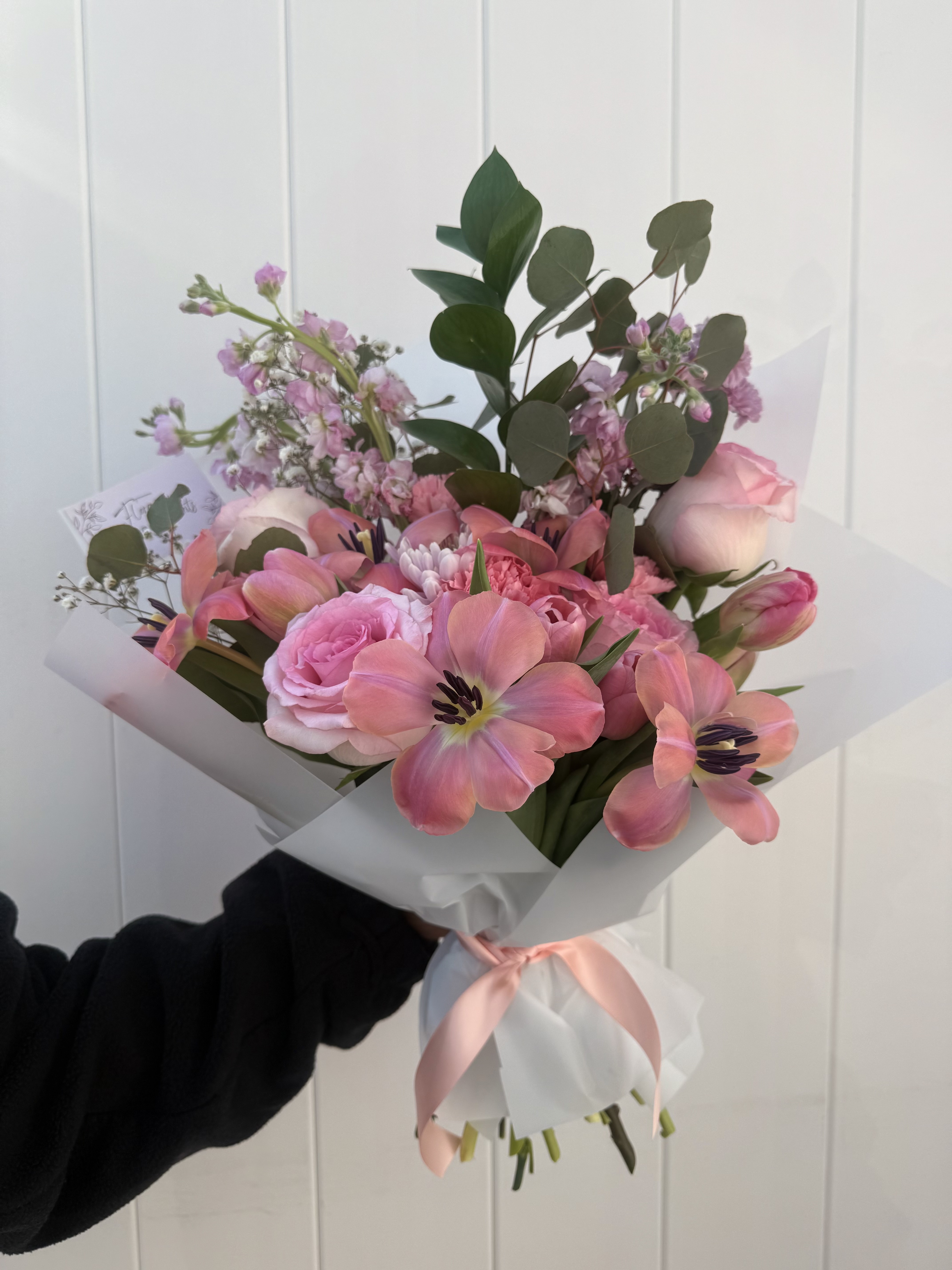 Soft pink bouquet with tulips, roses, and eucalyptus in white paper with pink ribbon