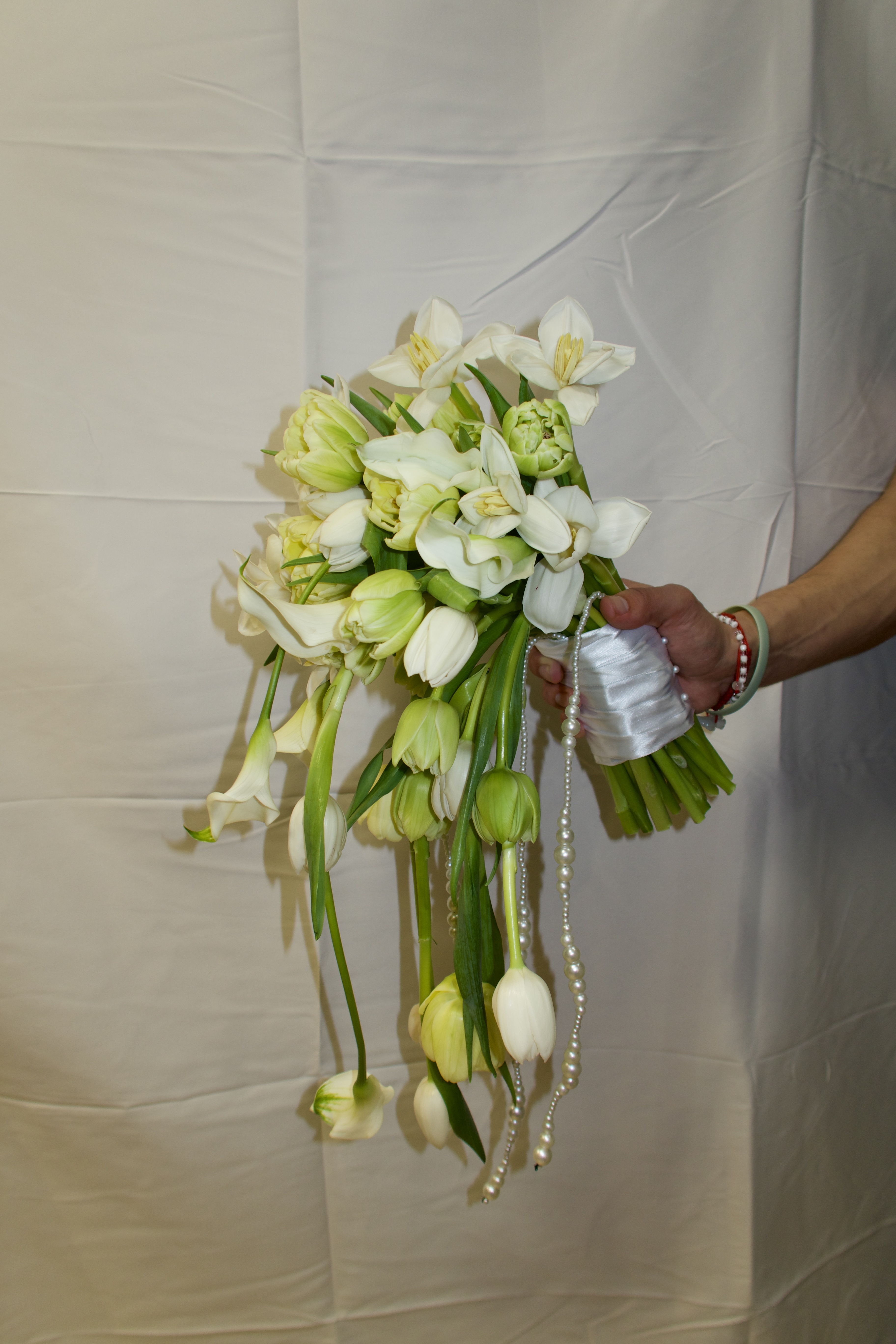 White and lime green cascade bridal bouquet with pearl strands held by person in white