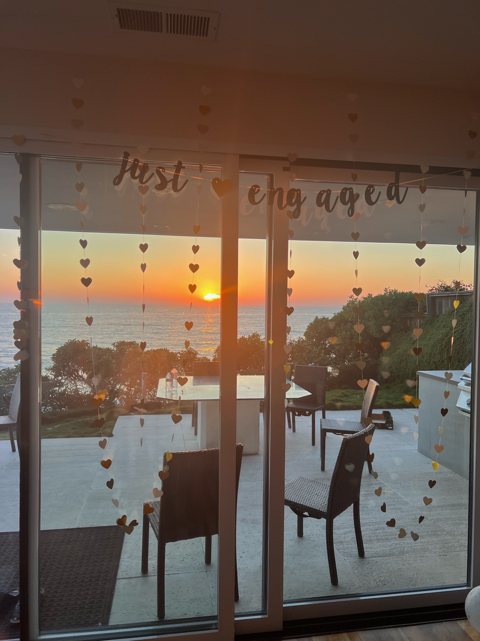 Sunset engagement celebration with 'just engaged' banner and heart decorations overlooking ocean