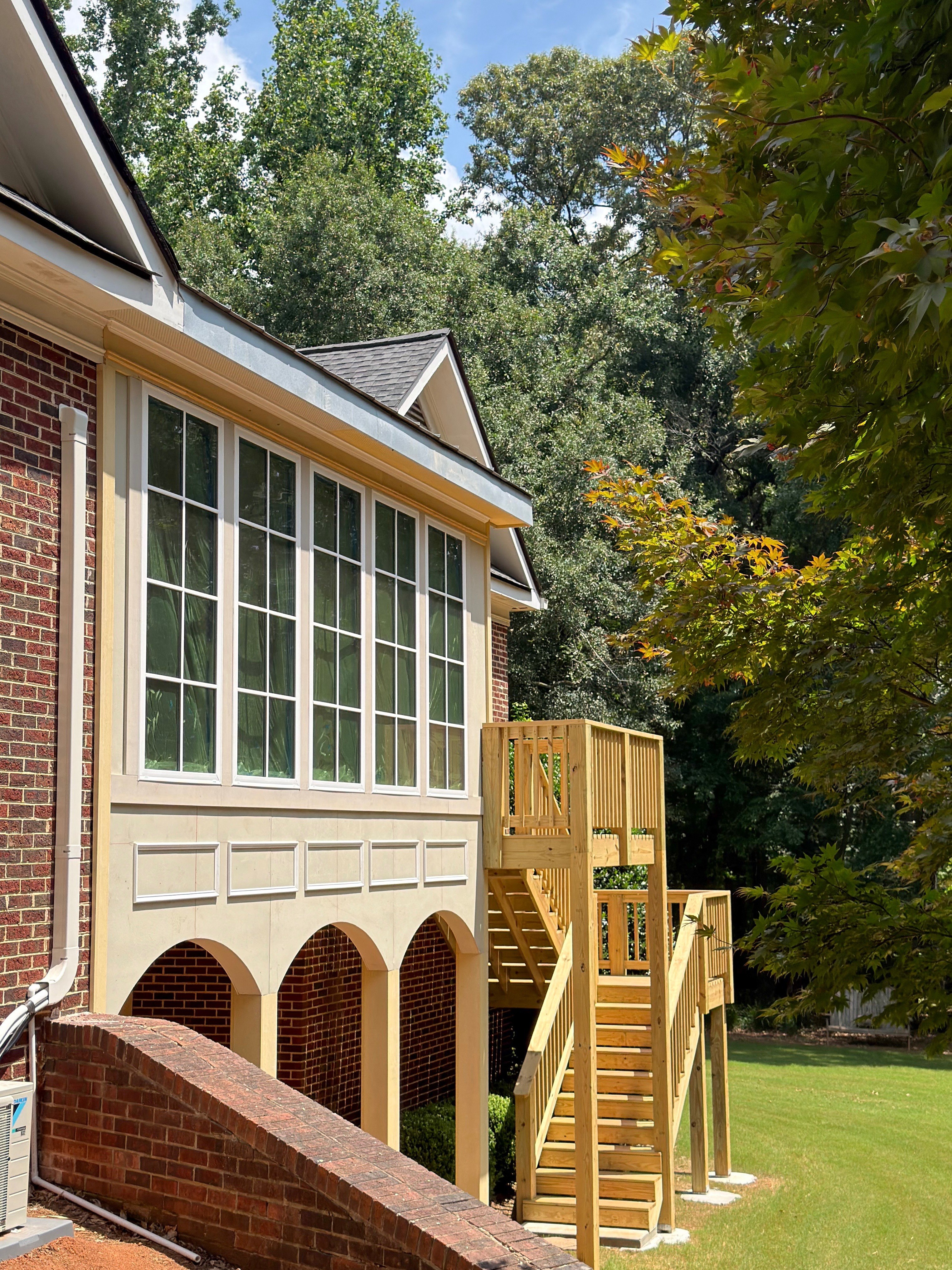 Sunroom addition with a wall of divided-light windows above a new elevated wood deck and staircase off a brick home