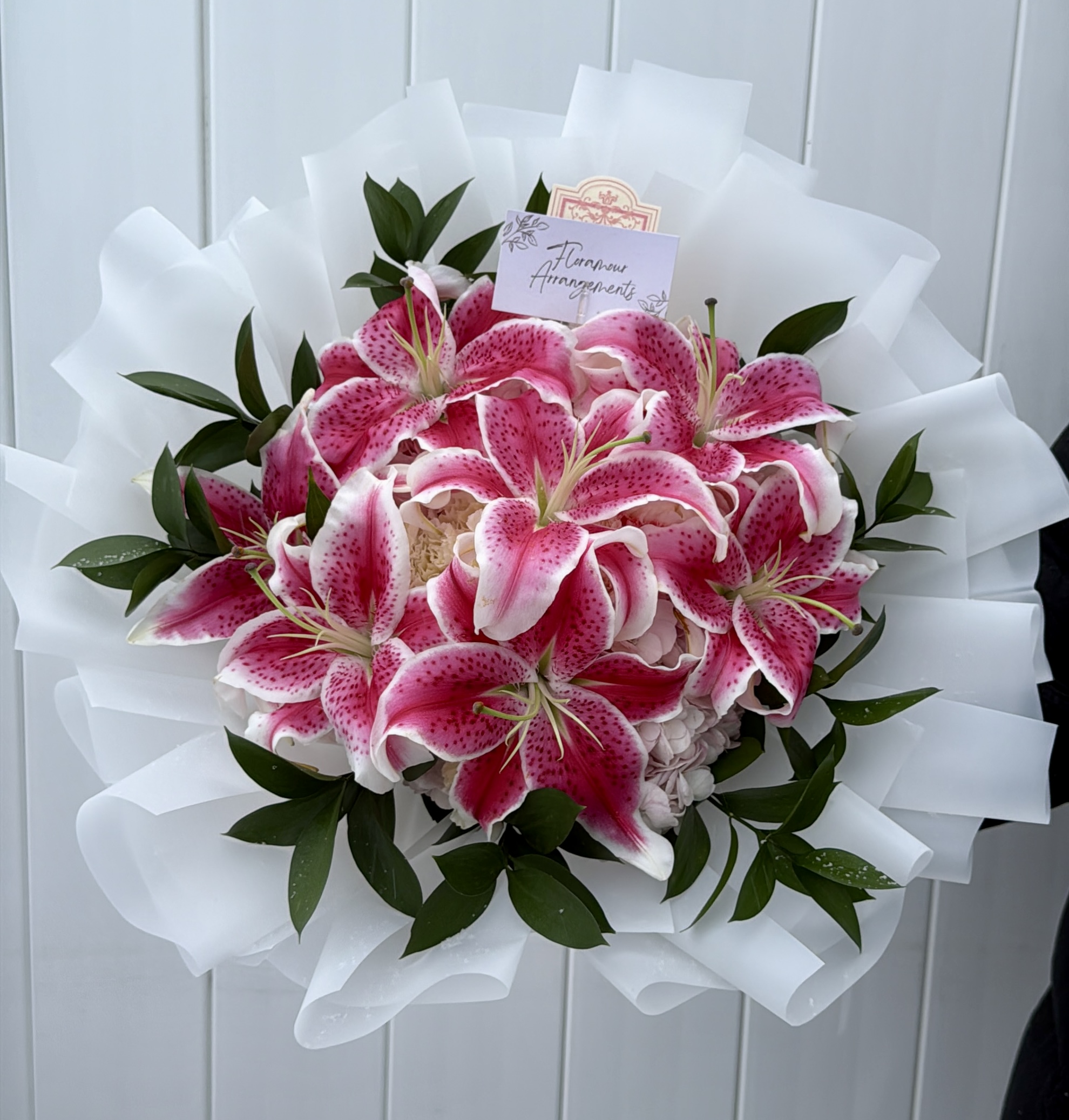 Pink stargazer lily bouquet wrapped in white tissue with greenery