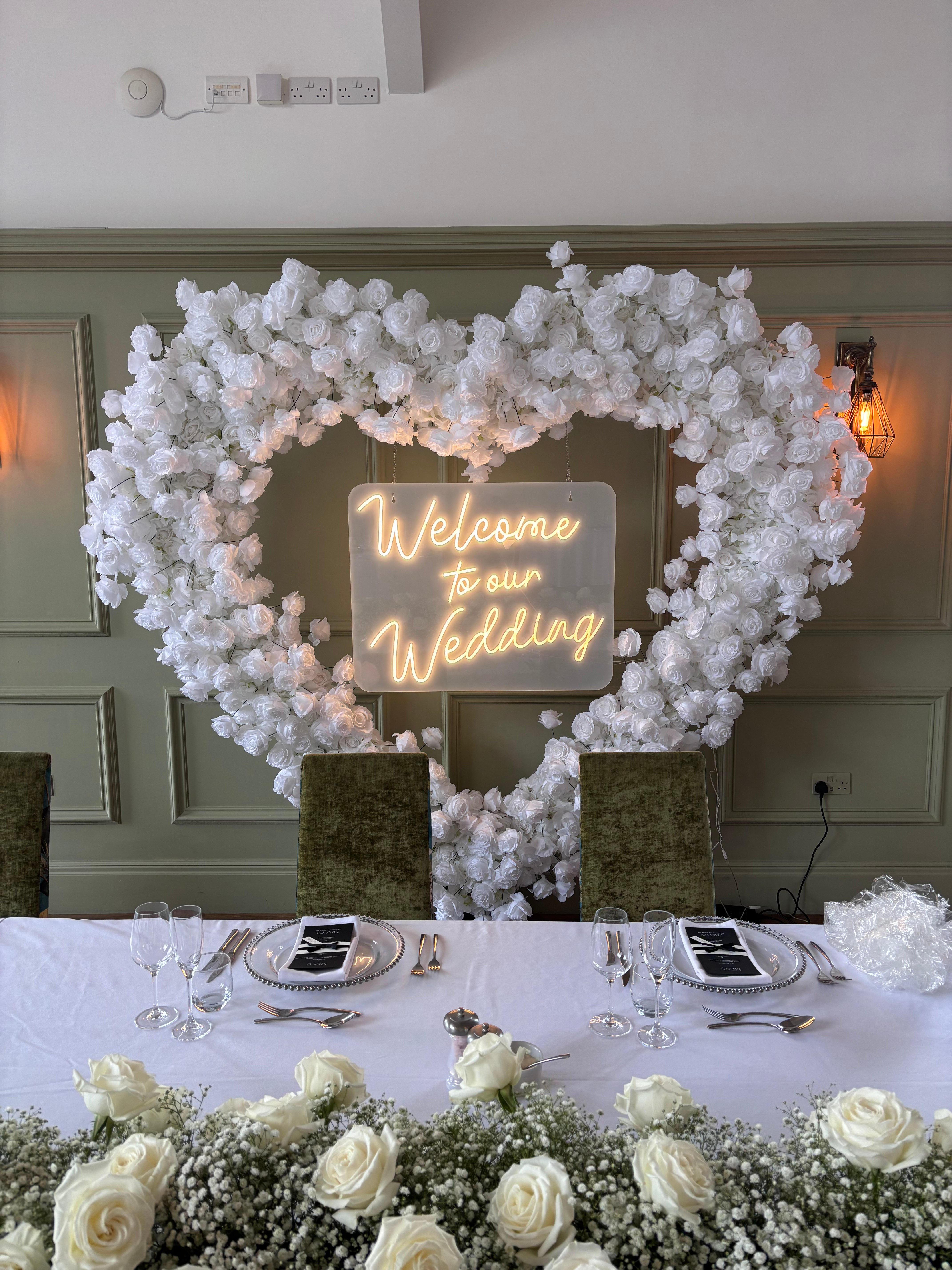 Heart-shaped white flower wall with Welcome to our Wedding neon sign