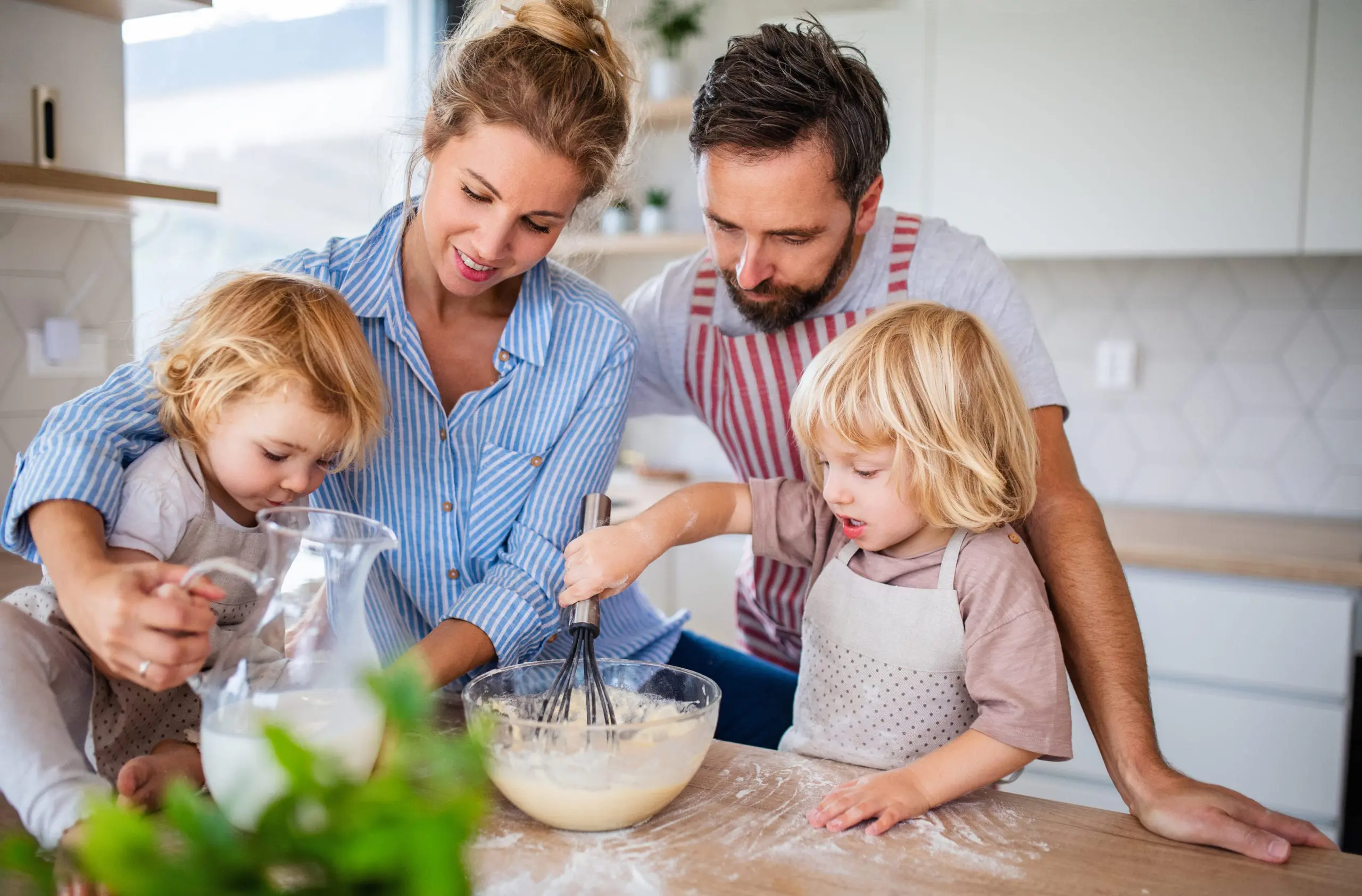 Parents and two young children mixing batter together in a bright kitchen