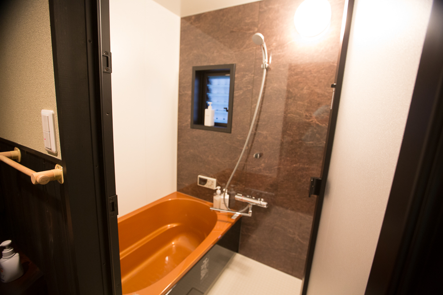 Modern bathroom with amber-colored soaking tub, brown marble accent wall, and handheld shower