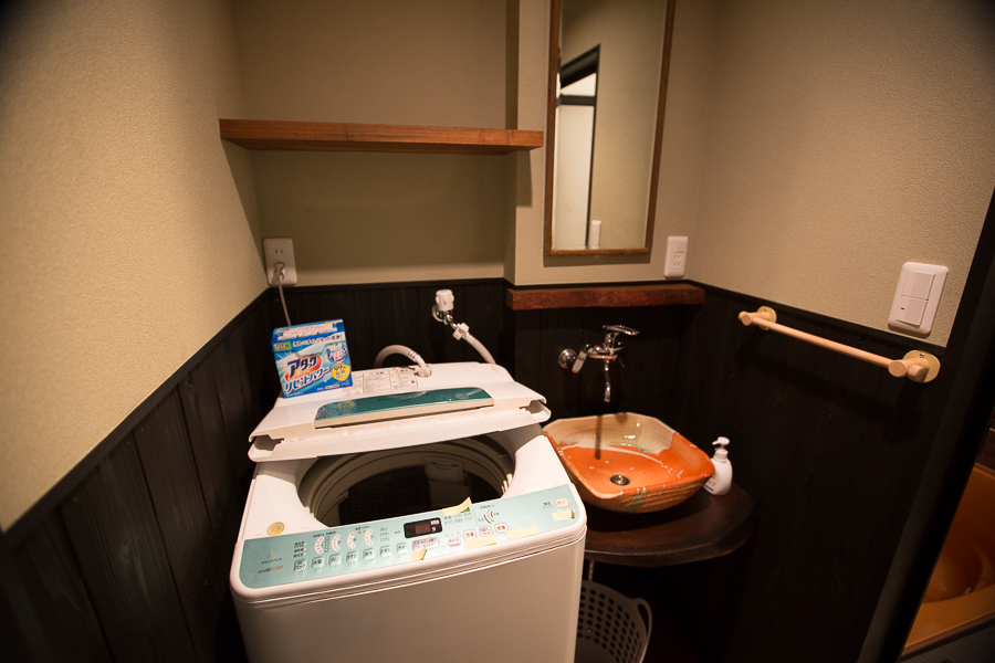 Laundry room with washing machine, decorative orange ceramic vessel sink, and dark wood wainscoting