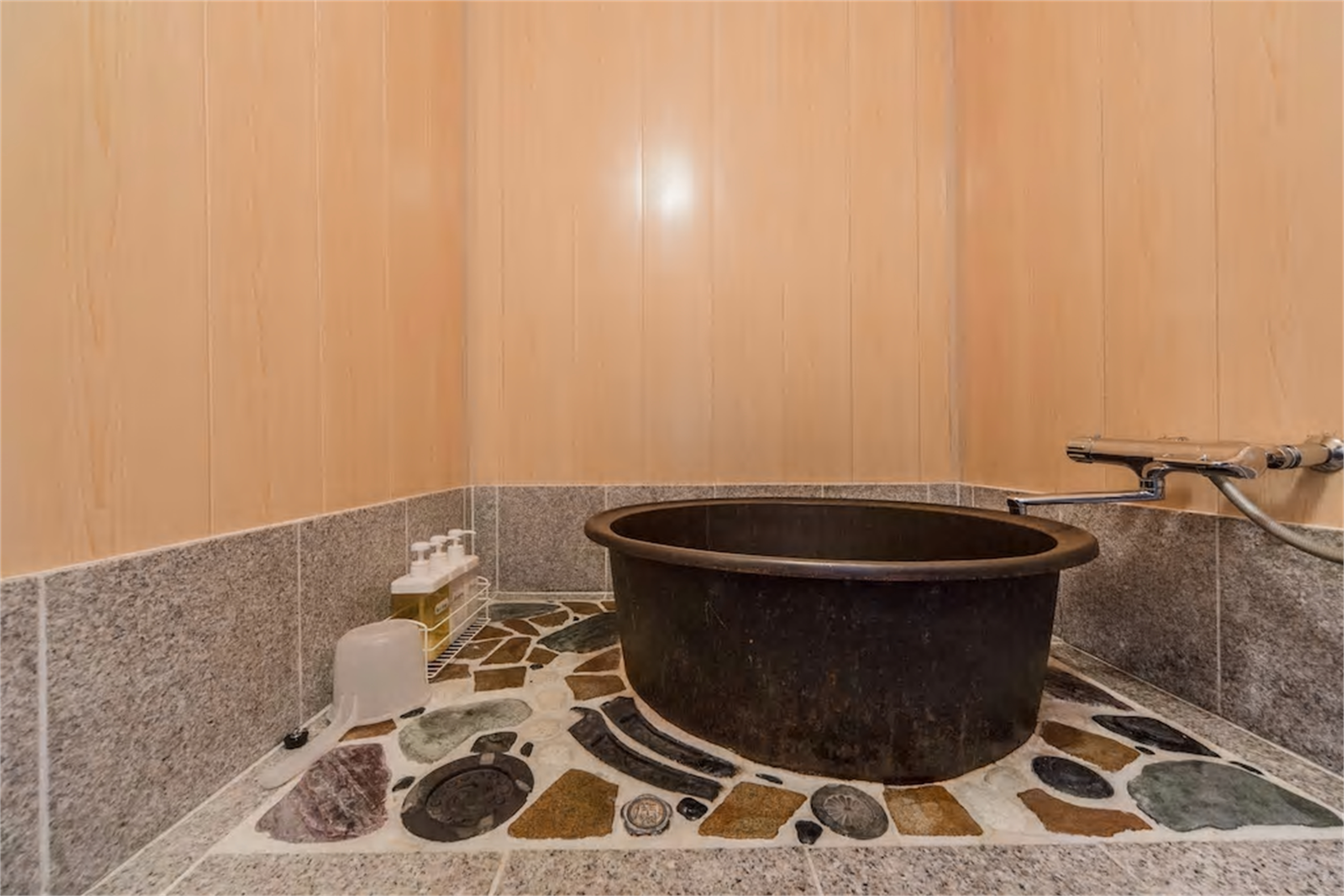 Traditional bathroom with deep black ceramic goemon tub, colorful polished stone mosaic floor, hinoki wood paneling