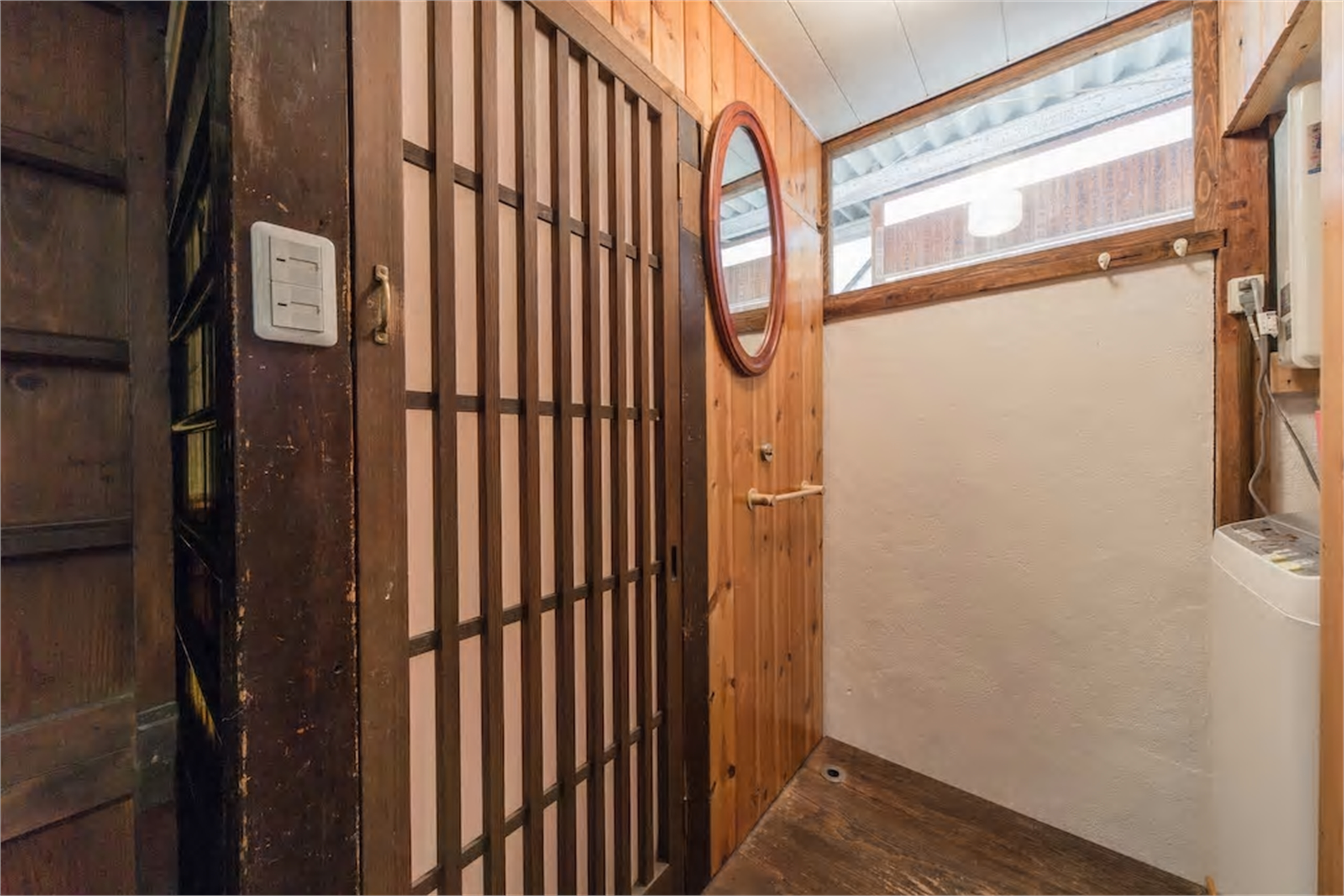 Machiya hallway with dark wooden lattice closet doors, cedar paneling, circular red-framed mirror, and clerestory window