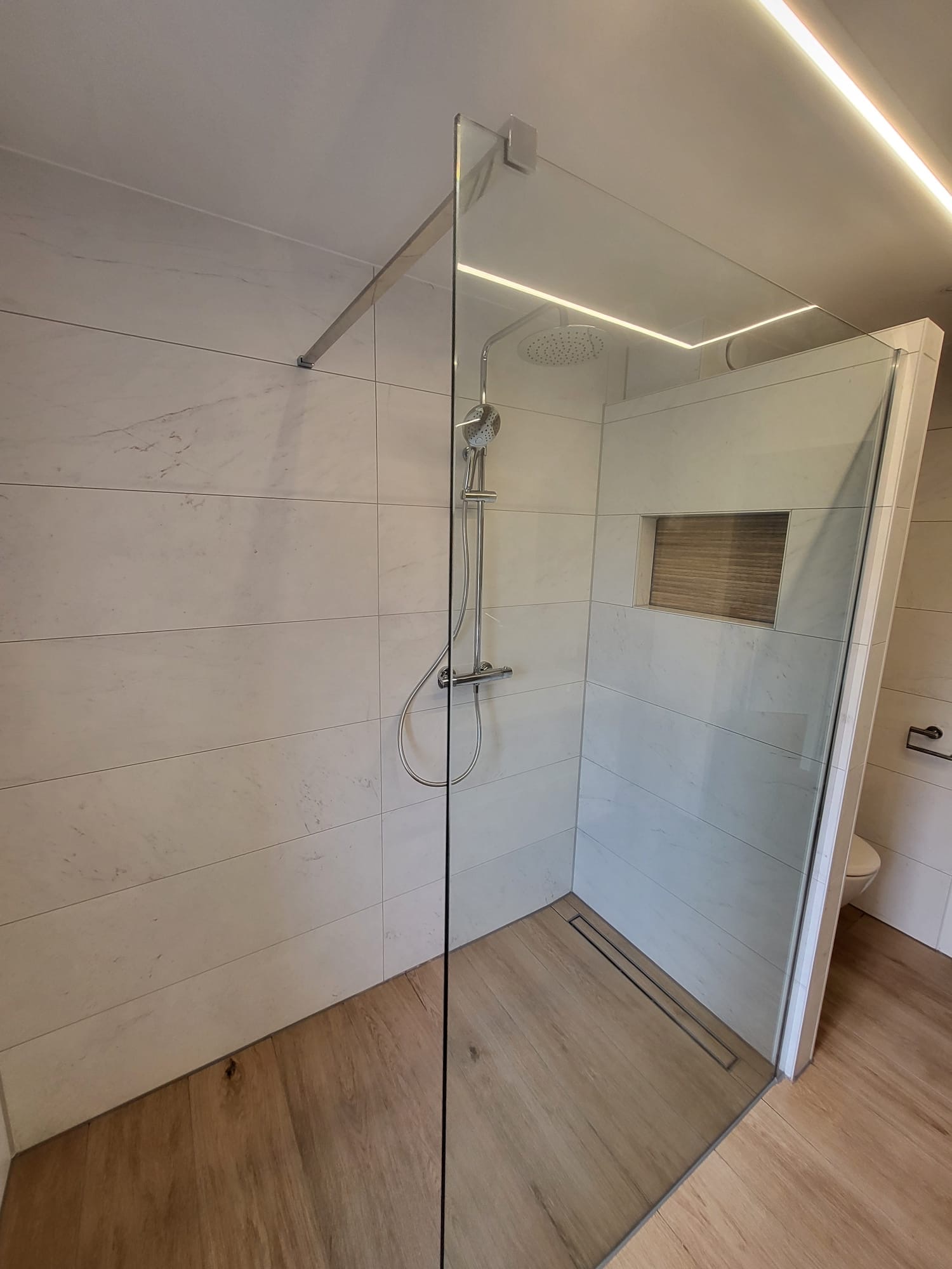 Inloopdouche met witte marmerlook tegels, glazen wand, douchegoot en houtlook vloertegels