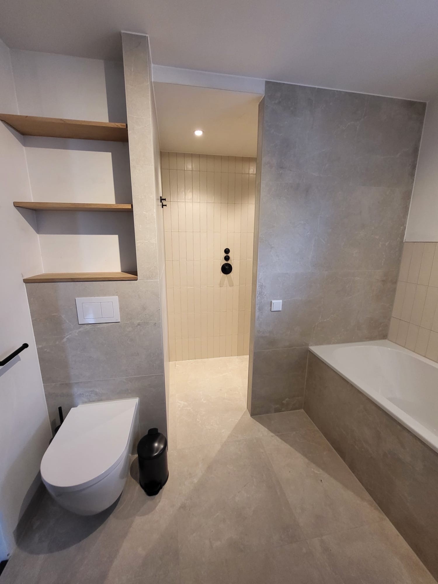 Badkamer met hangtoilet, houten wandplanken, ingebouwd bad en inloopdouche met crèmekleurige staande tegels