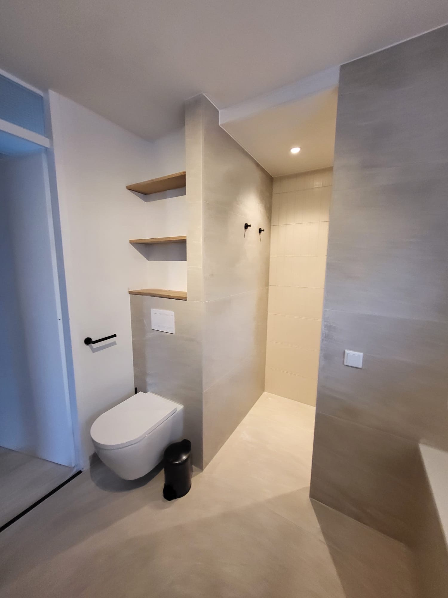 Hangtoilet naast een betegelde douchewand met houten planken in een wandnis