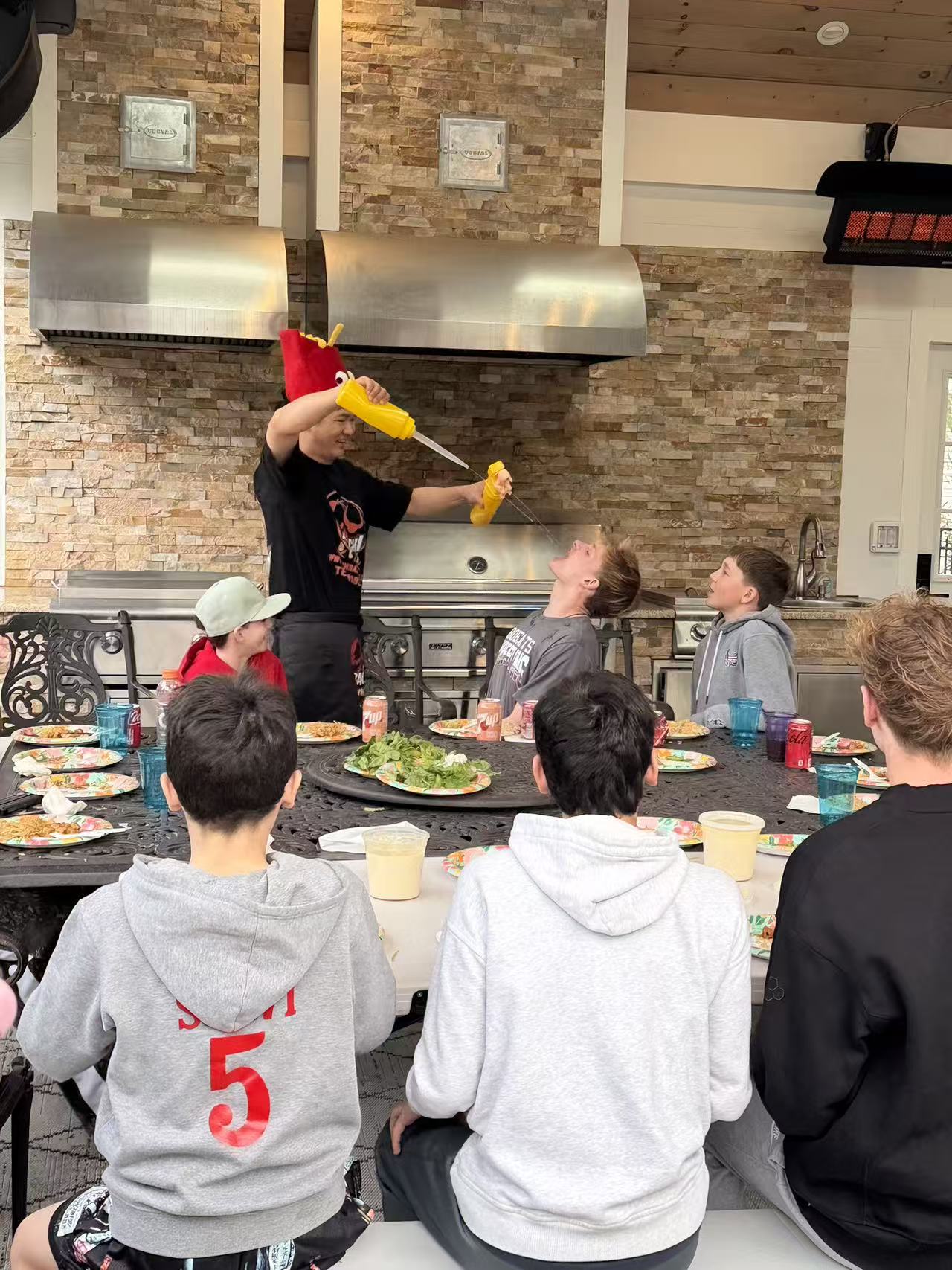 Hibachi chef performing the classic mustard squirt trick with kids at a backyard party