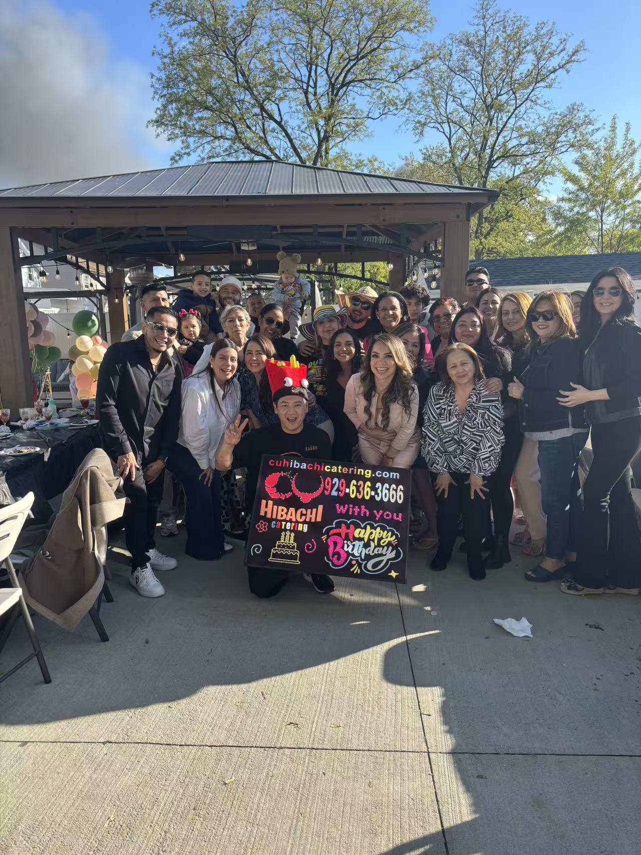 Large family group photo at pavilion with colorful LED birthday sign
