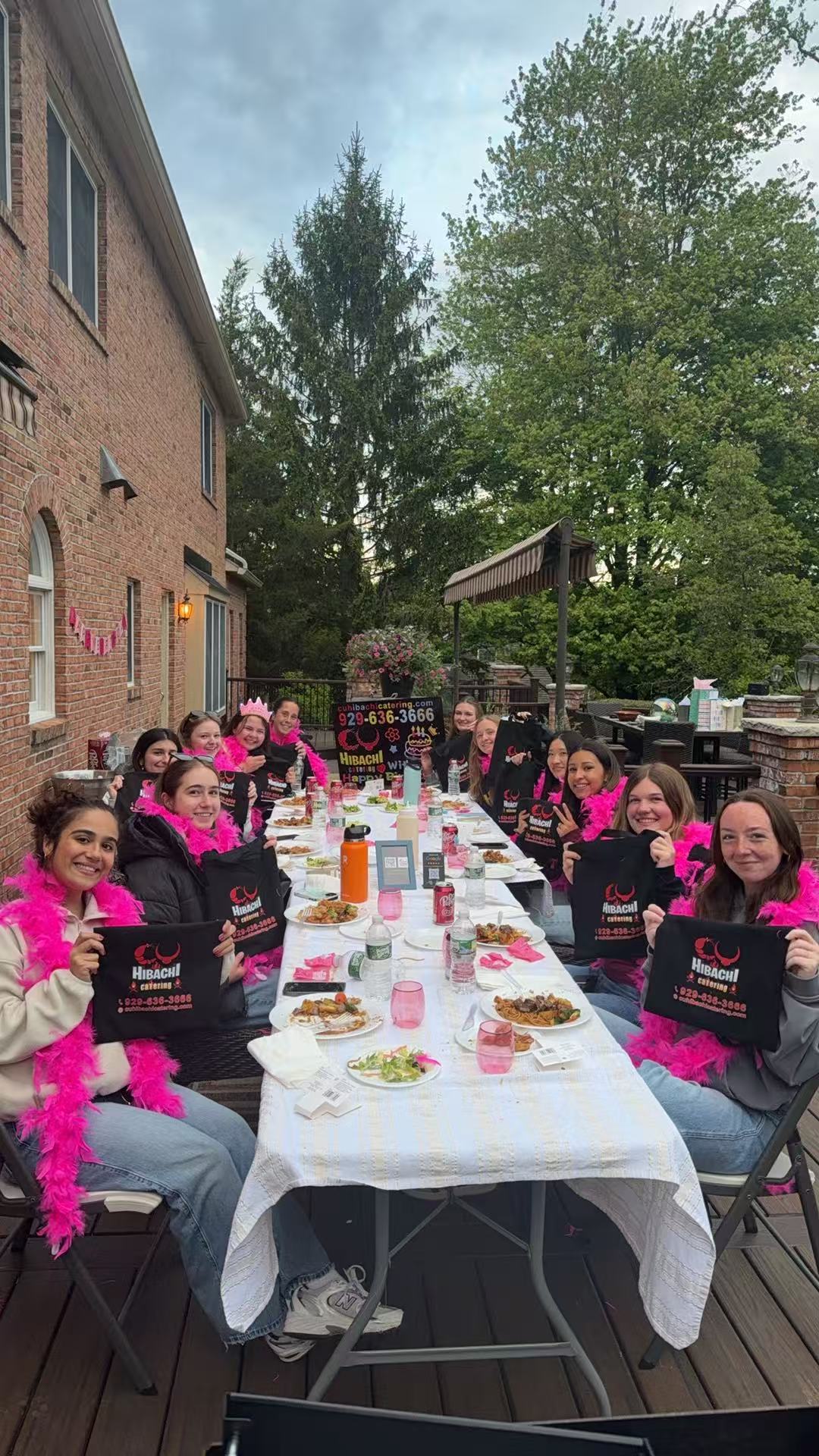 Bachelorette party guests holding CU Hibachi Catering bags with pink feather boas at outdoor dinner
