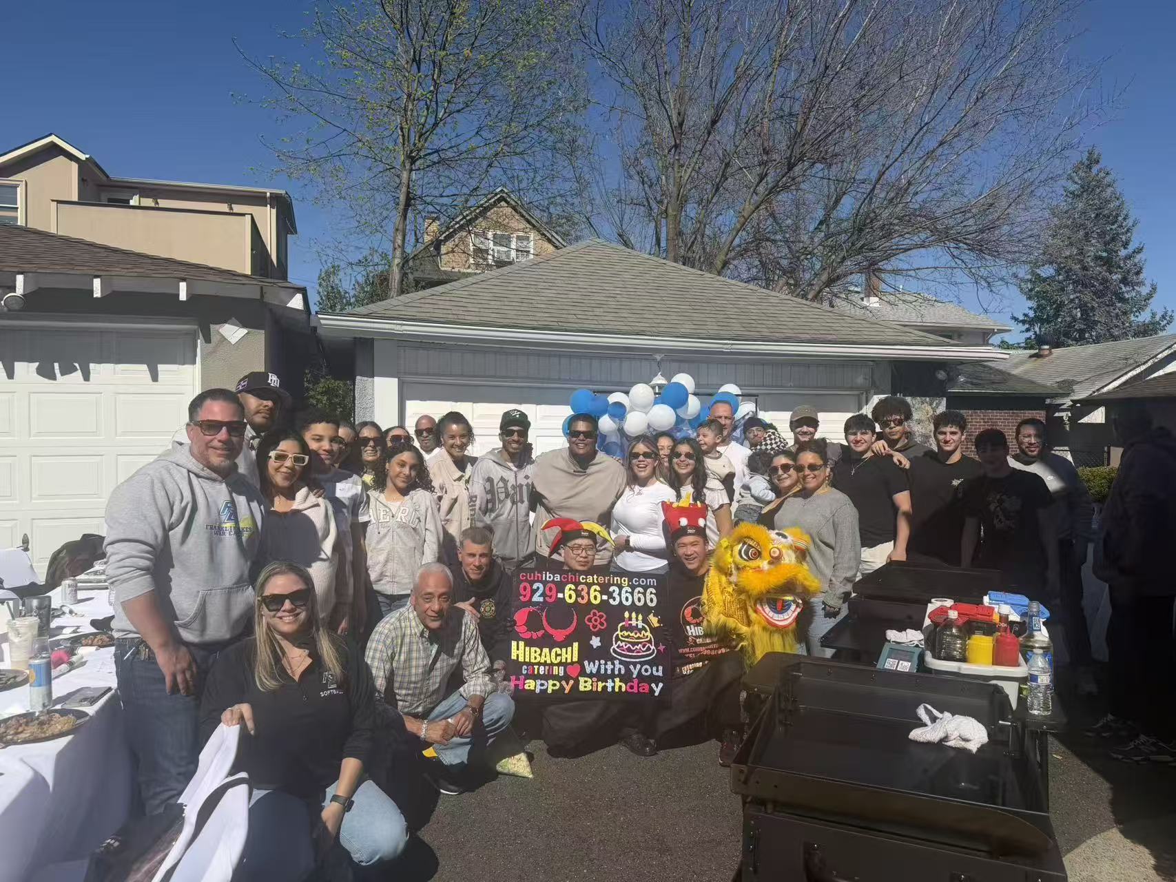 Large group photo with lion dance costume and blue balloons at outdoor party