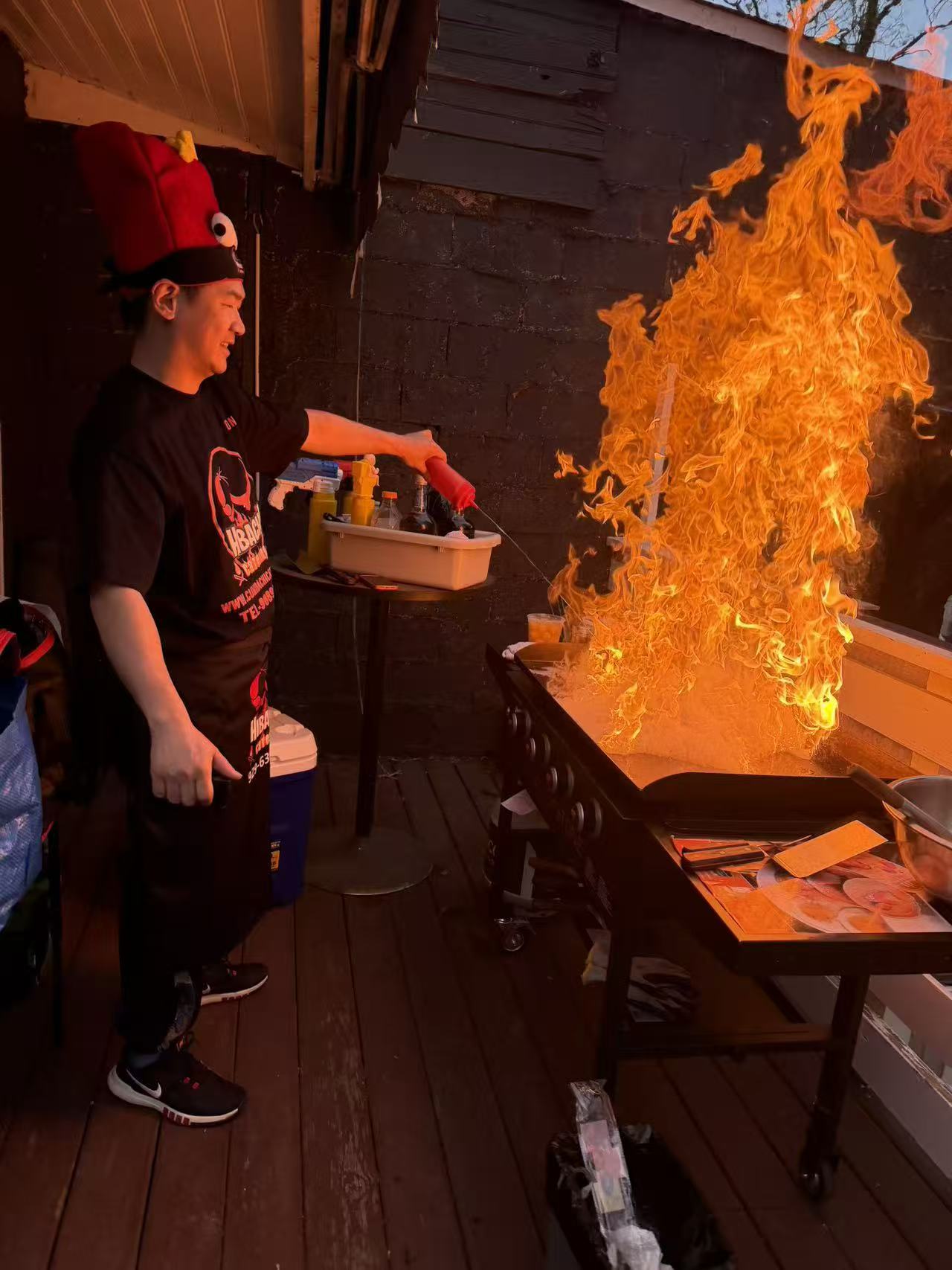 Hibachi chef with red lobster hat performing dramatic fire show on backyard deck