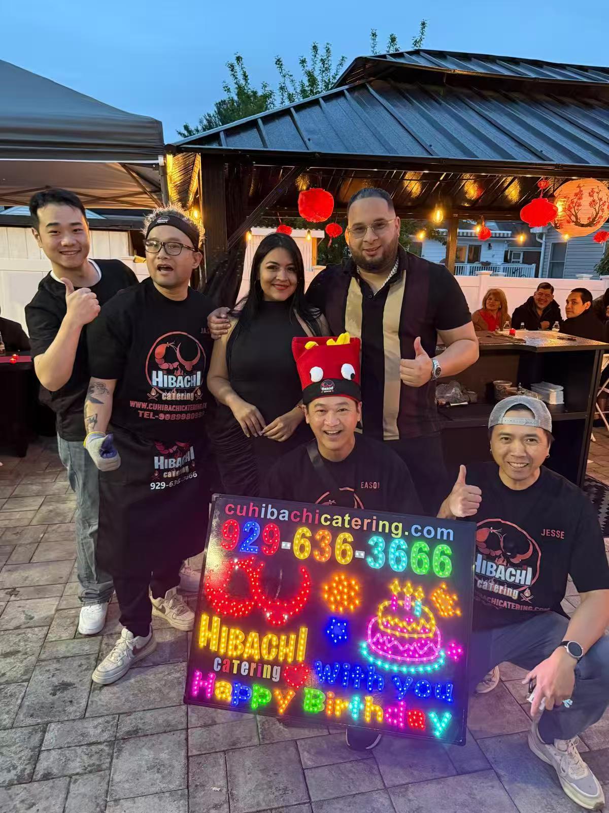CU Hibachi Catering team posing with colorful LED birthday sign at evening event