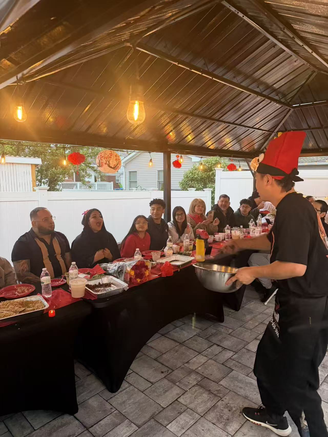 Chef serving family at covered patio party with red lanterns and string lights
