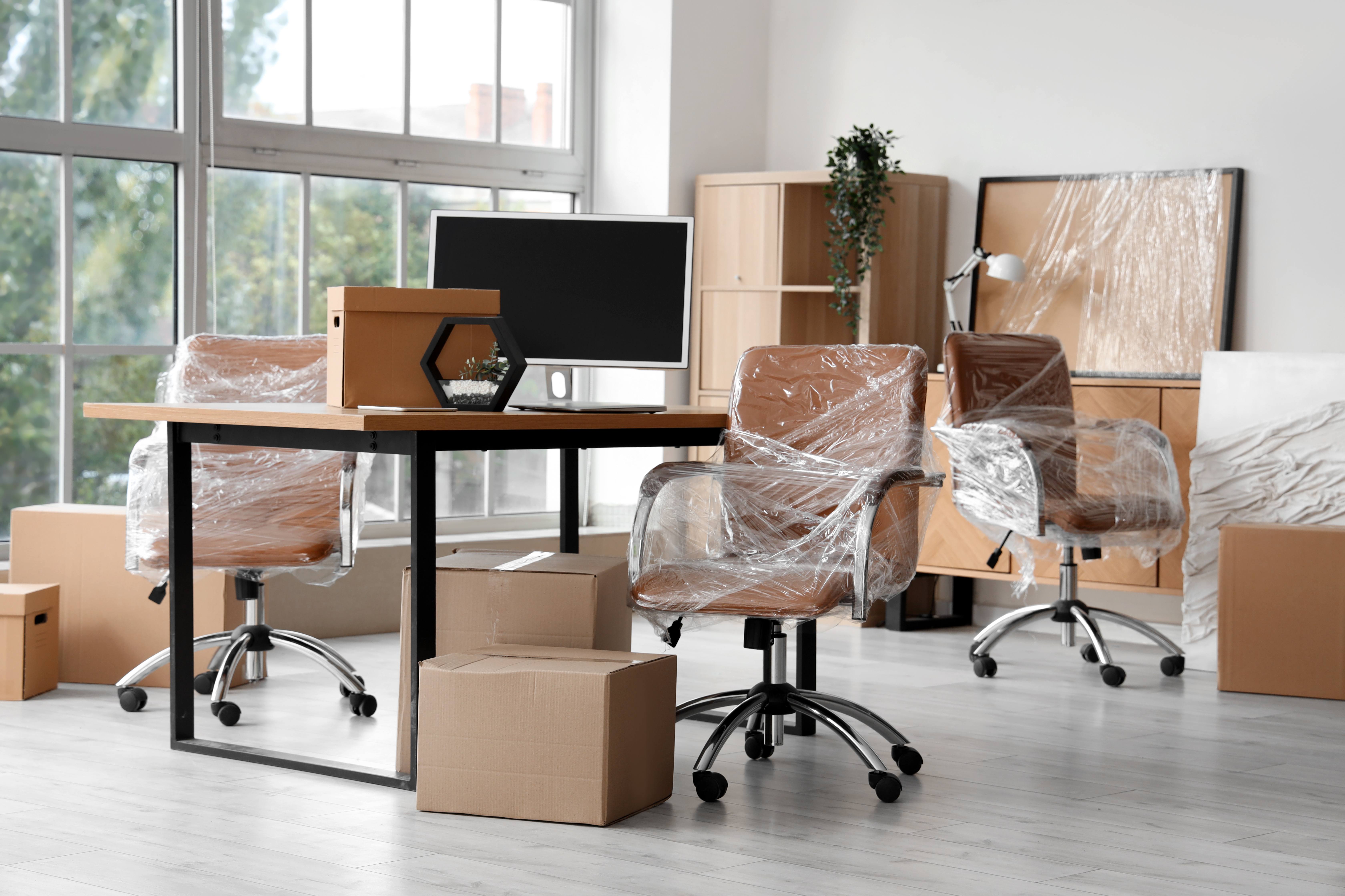 Modernes Büro mit verpackten Möbeln und Kartons beim Umzug
