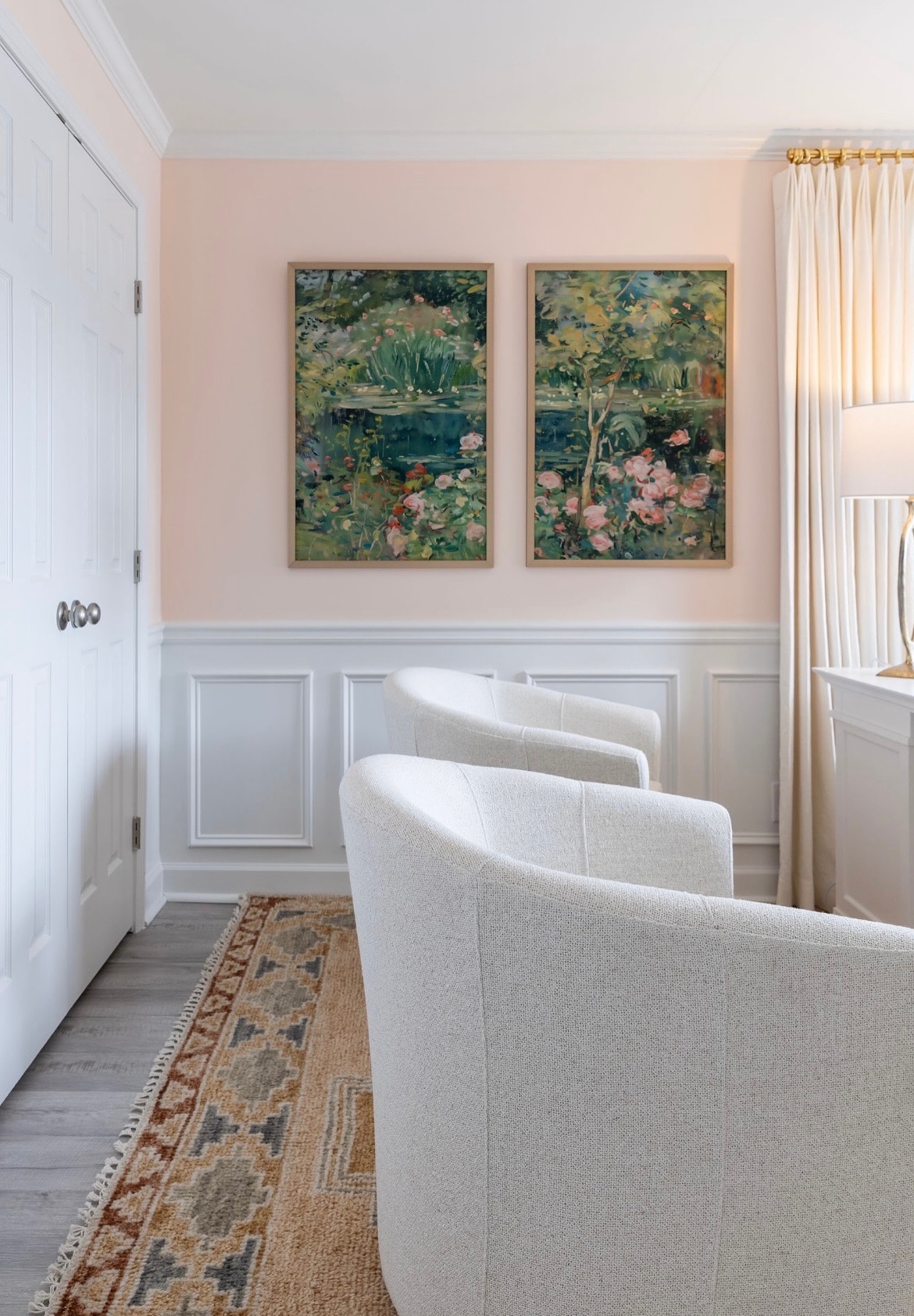 Blush sitting room with wainscoting, two framed garden paintings, and white swivel chairs