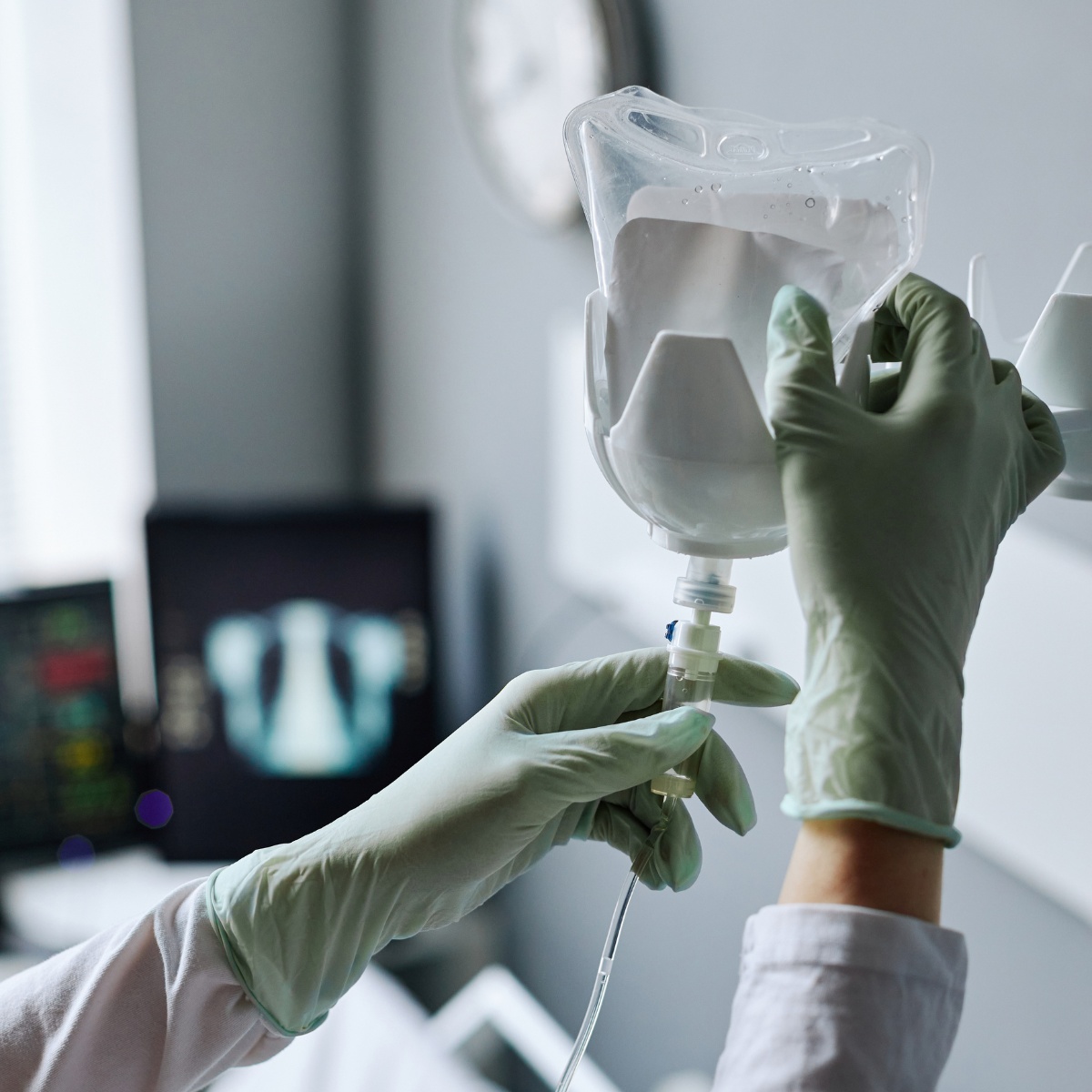 Gloved hands adjusting a clear IV hydration bag on a stand in a clinical setting