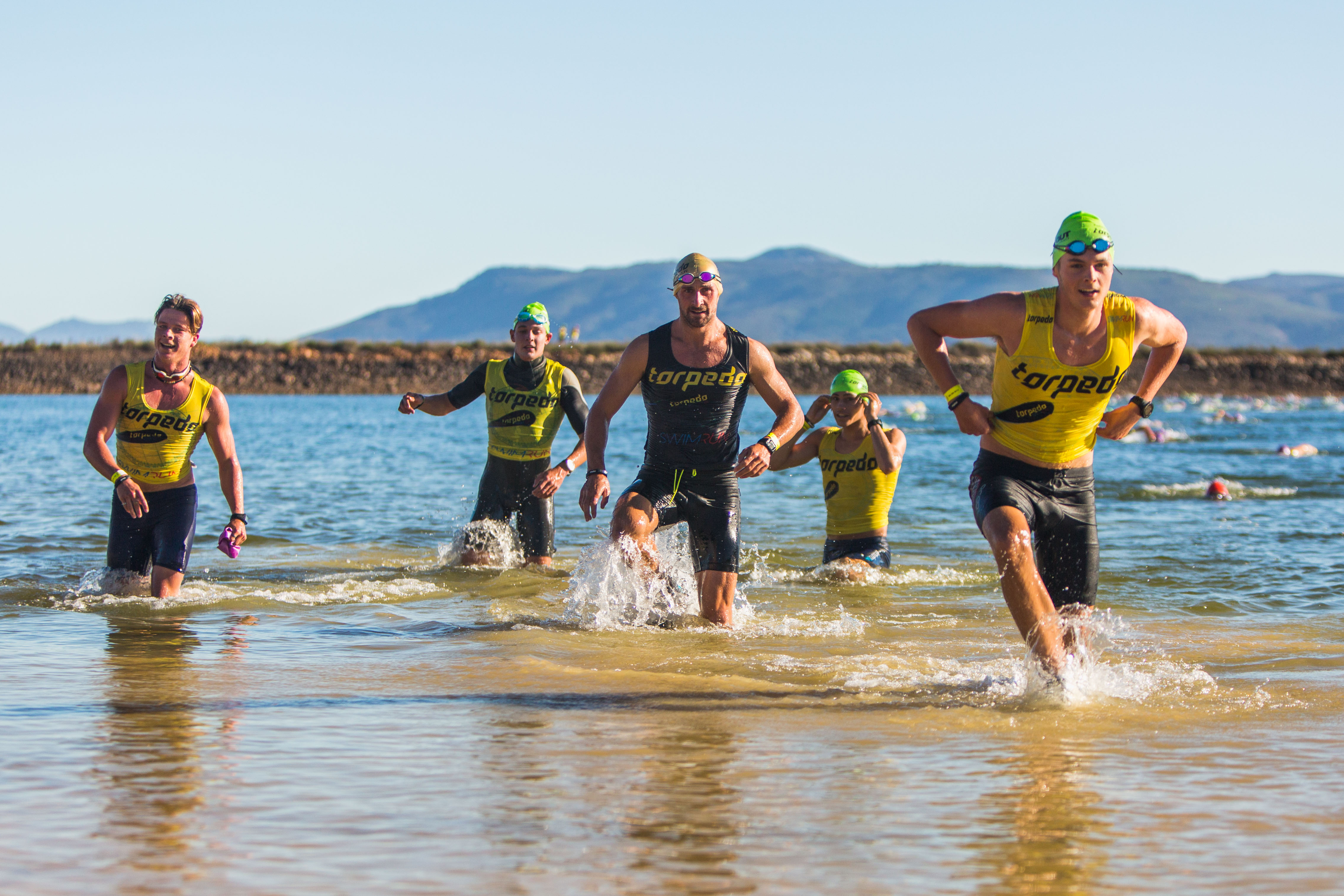 Group of athletes running out of shallow dam water splashing