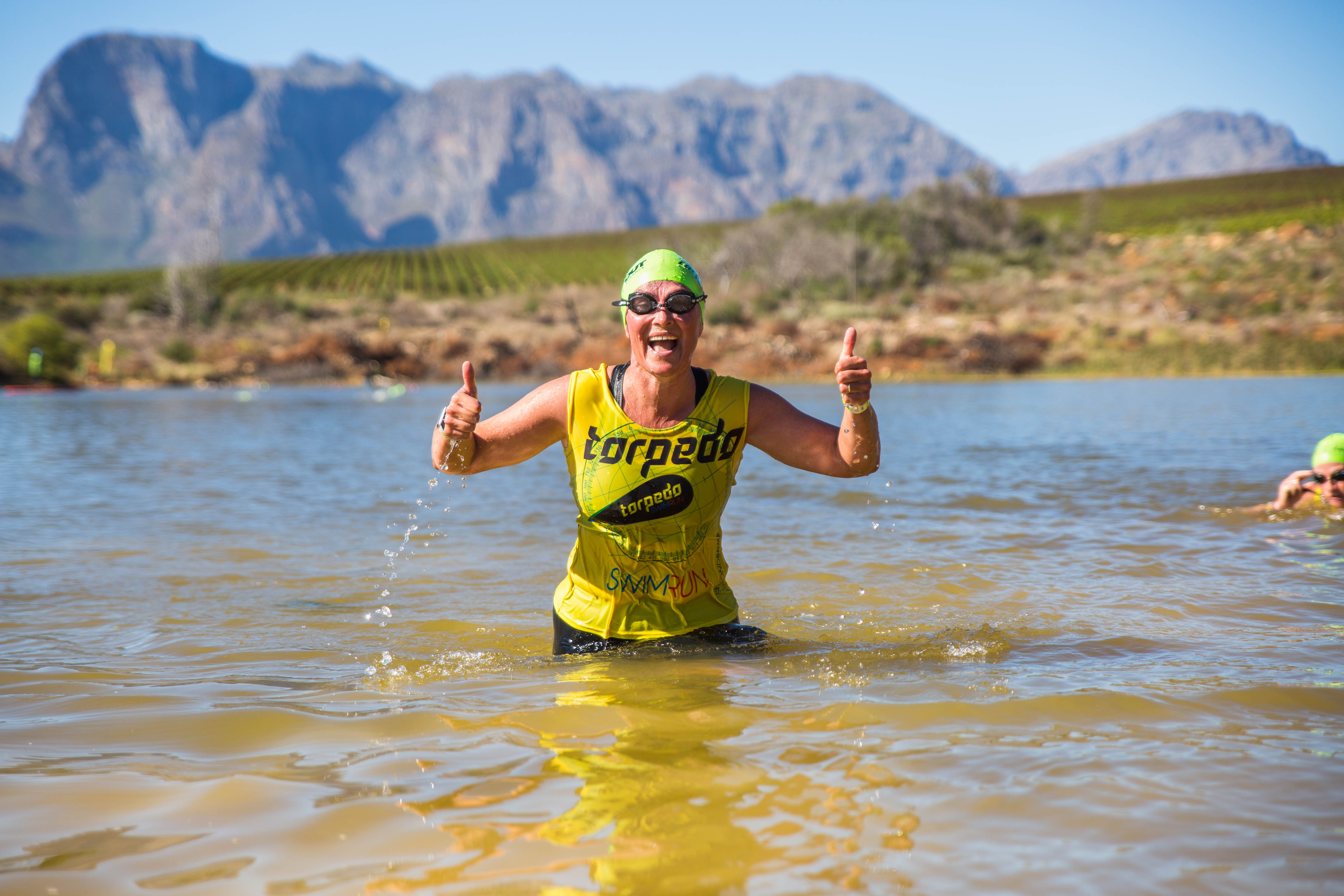 Athlete celebrating in the dam with thumbs up, mountains behind