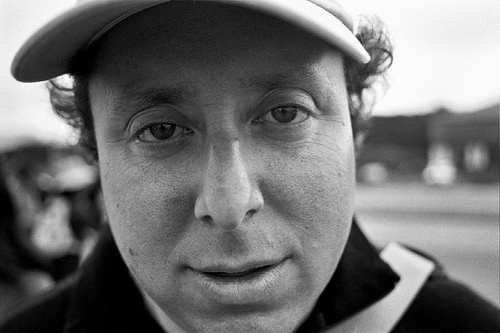 Portrait photograph of man wearing flat cap looking directly at camera with direct steady gaze