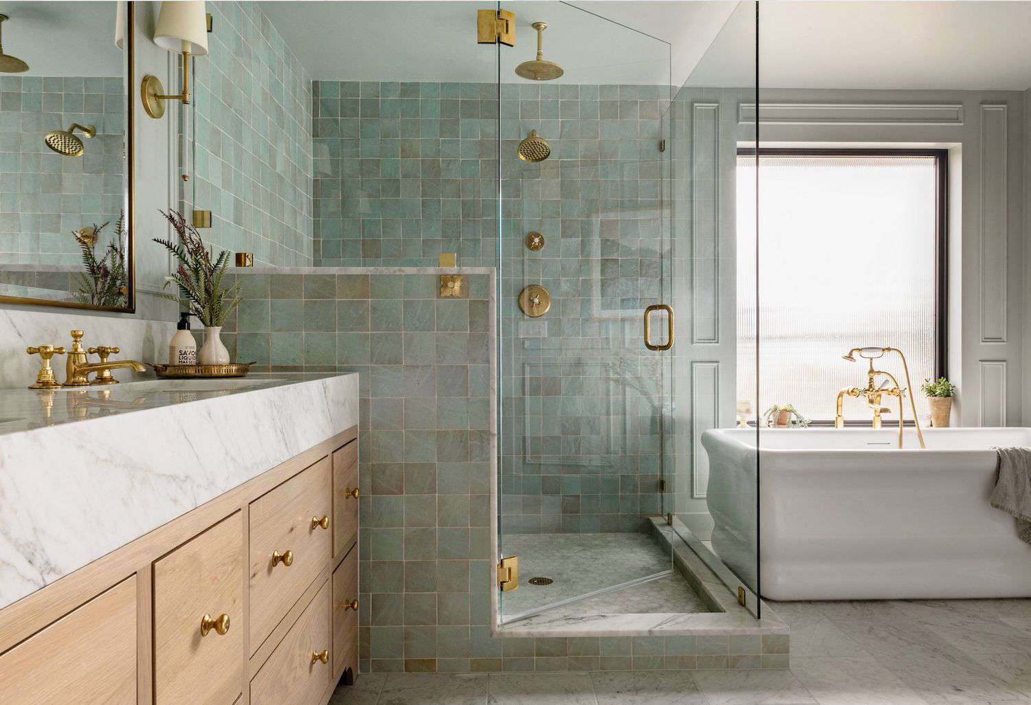 Luxury spa bathroom with sage-green tile shower, marble vanity, brass fixtures, frameless glass, freestanding tub by window