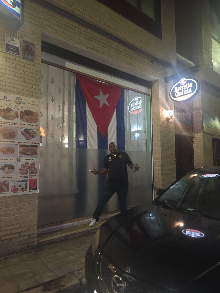 DJ JOHNX frente al restaurante D'Cuba con la bandera cubana