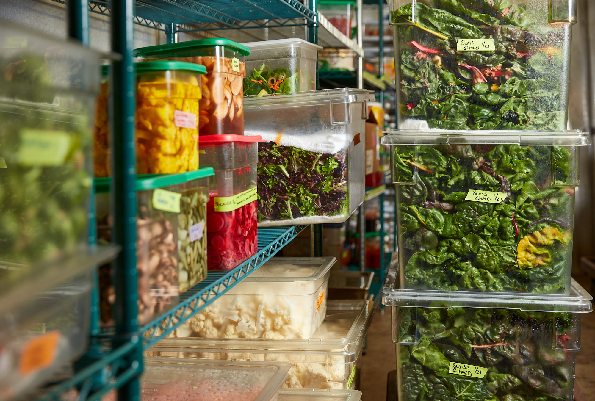 Labeled containers of fresh prepped produce on kitchen storage shelving